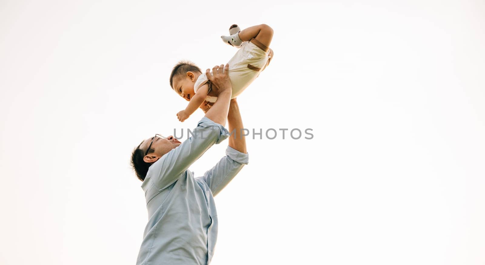 Father holds his baby daughter up high throwing up by Sorapop