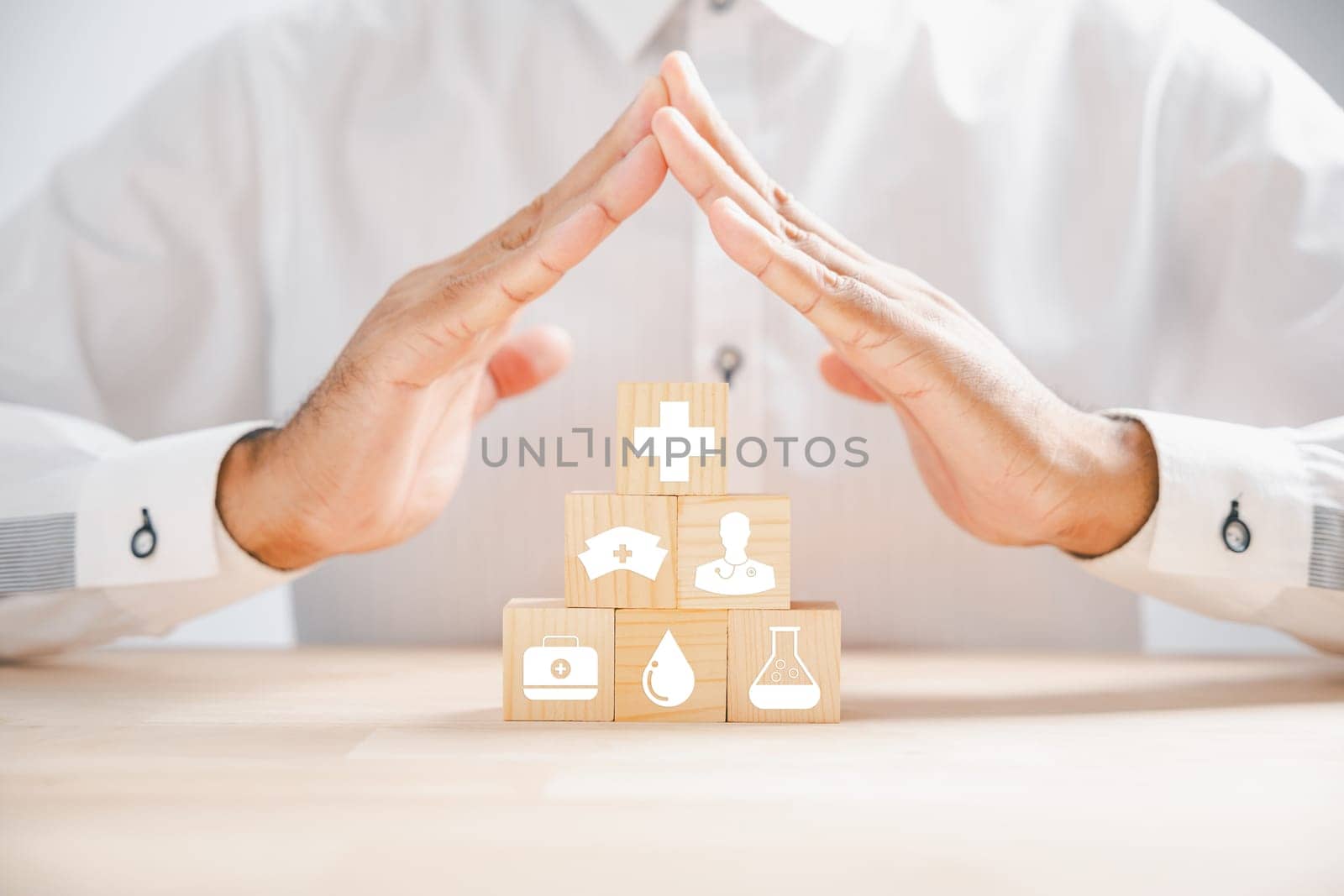 Healthcare insurance concept illustrated by stacked wooden cubes with medical icons, topped by a doctor hand showing protection sign. Ensuring a safe medical future. Health care concept