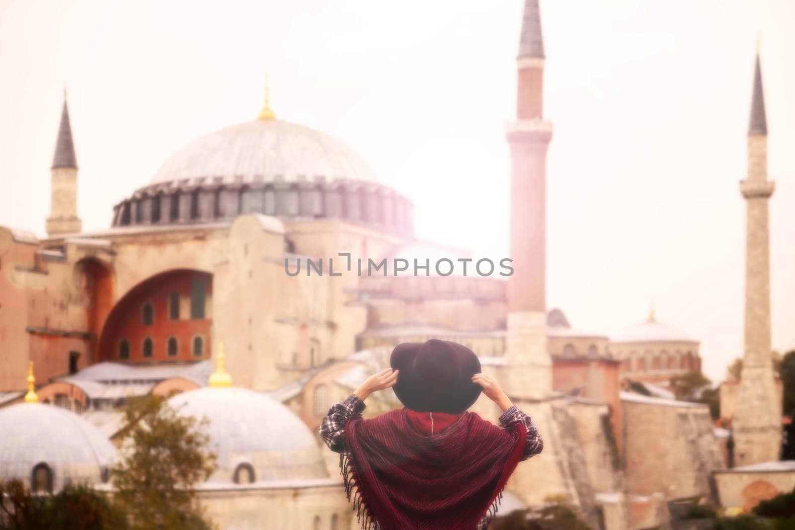 A young pretty girl in a stylish hat and a plaid shirt poses, makes a selfie on the phone next to the Hagia Sophia mosque. Tourism in Istanbul, Turkey.