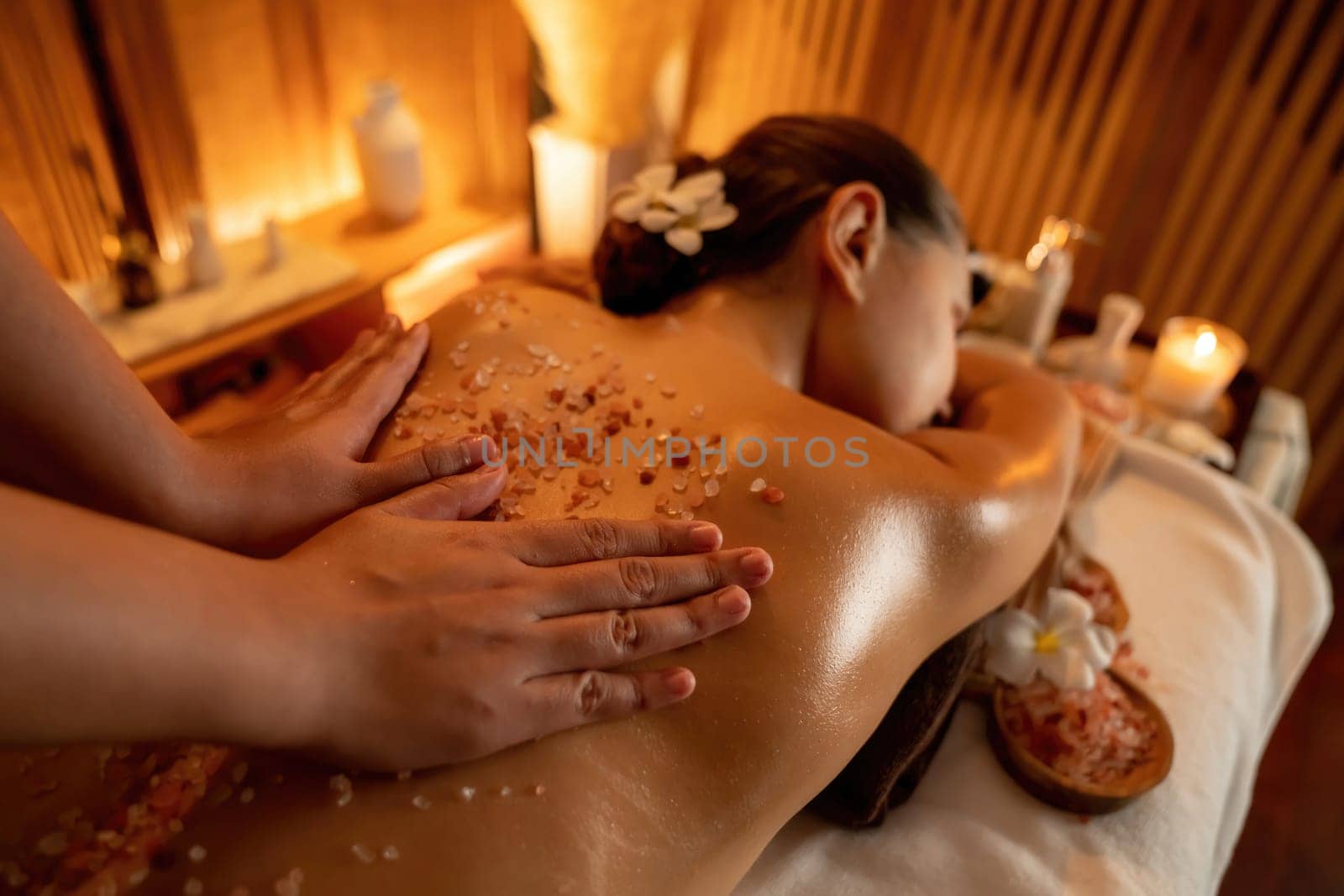 Woman customer having exfoliation treatment in luxury spa salon with warmth candle light ambient. Salt scrub beauty treatment in Health spa body scrub. Quiescent