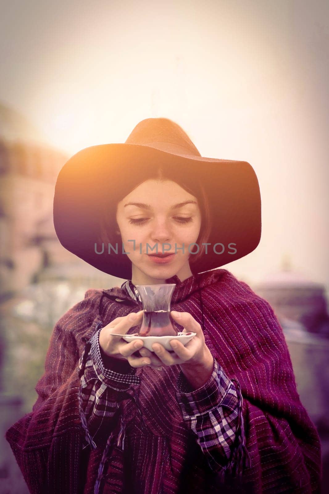 A young girl in a hat and poncho holds traditional Turkish tea by africapink