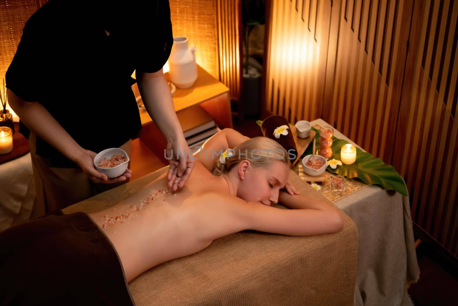 Woman customer having exfoliation treatment in luxury spa salon with warmth candle light ambient. Salt scrub beauty treatment in Health spa body scrub. Quiescent