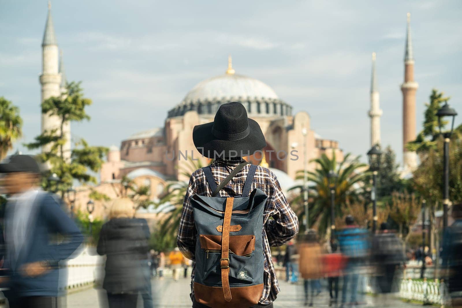 A young girl in a plaid shirt, with a stylish backpack and a hat and looks at the Hagia Sophia mosque at sunset. Istanbul, Turkey.