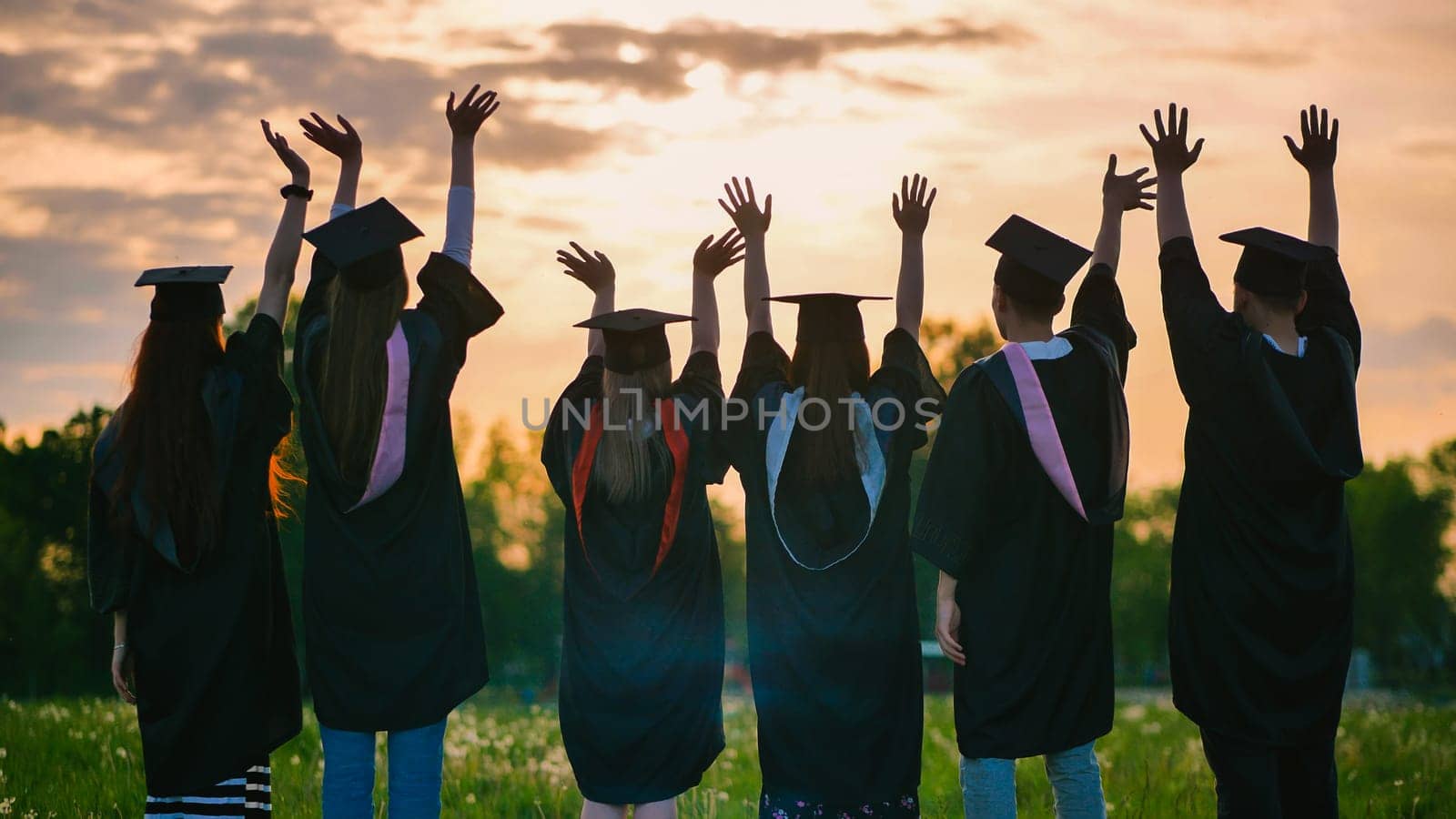 Silhouettes of graduates in suits at sunset waving to the sun