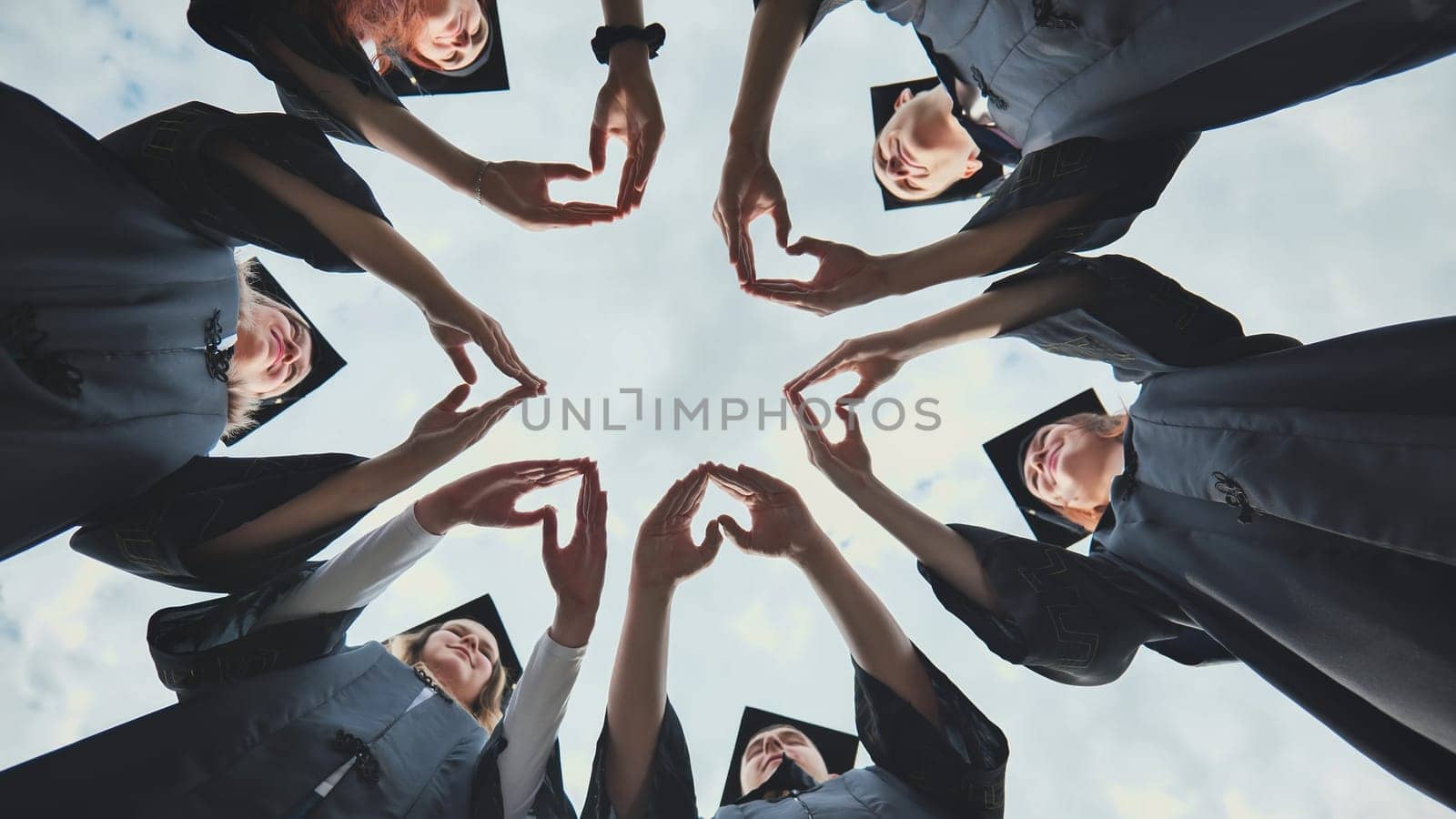 A group of college graduates stand in a circle and make hearts out of their palms. by DovidPro