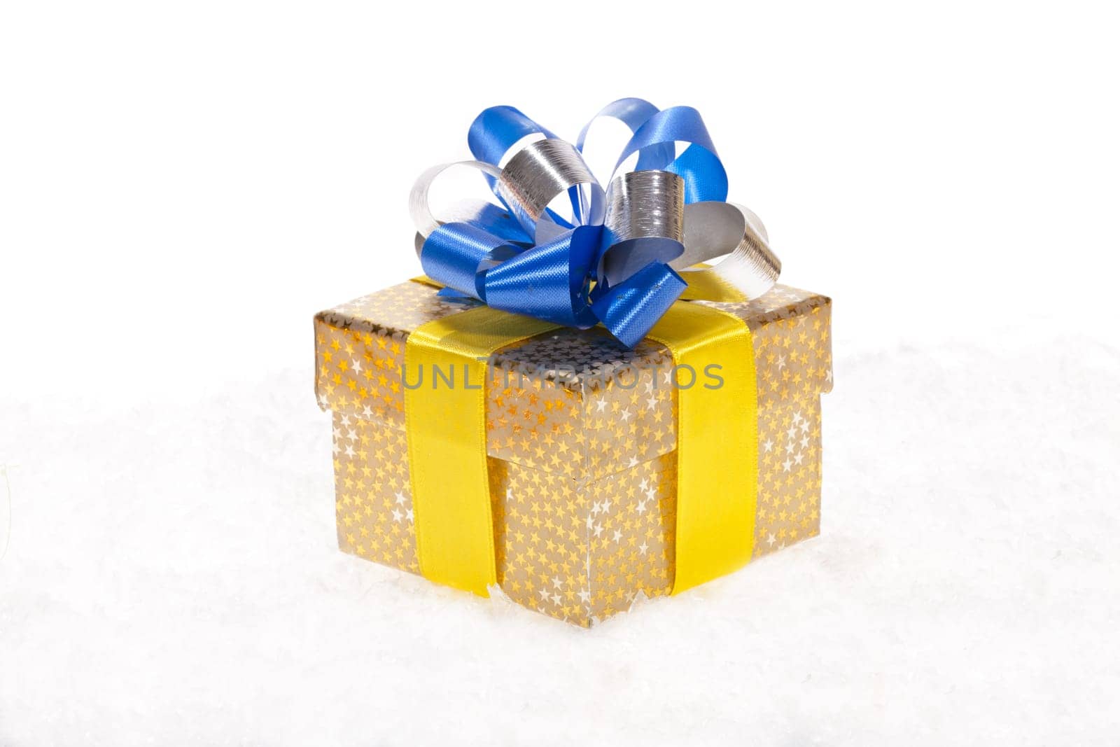 Golden Christmas package with blue syllable ribbon lying in the snow against white background
