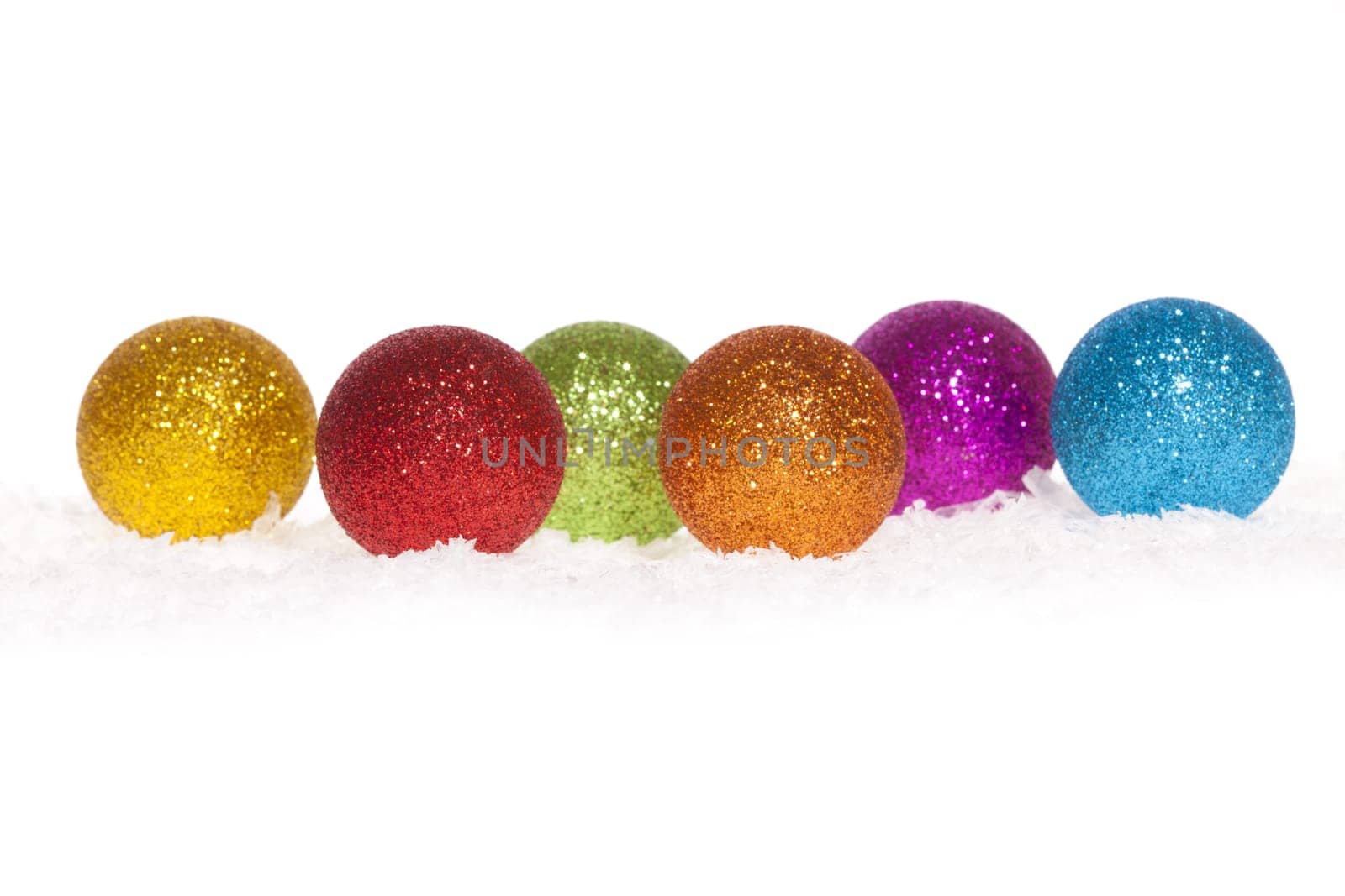 Colorful shiny Christmas tree baubles lying in the snow against white background