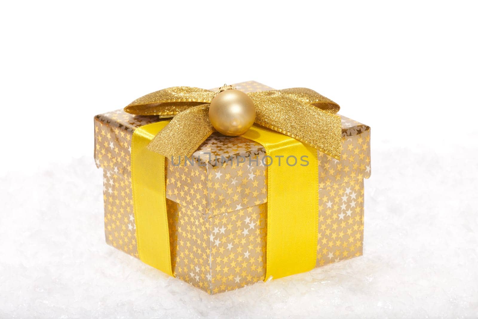 Christmas package with bow and golden ball lying in the snow against white background