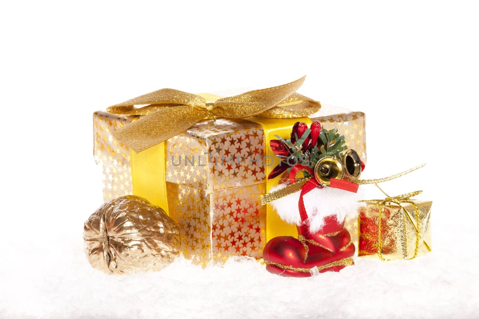 Package with bow,golden walnut and a red Santa boot lying in the snow against white background