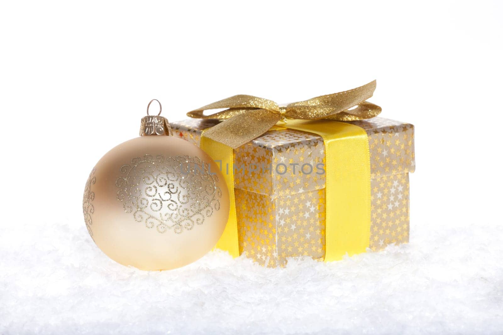 Package with bow and big golden balls lying in the snow against white background