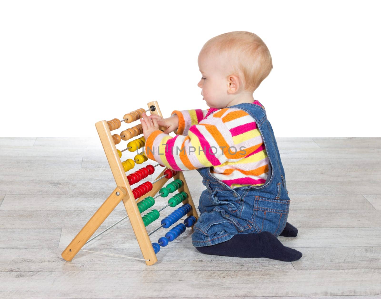 Cute little baby girl kneeling on the floor in dungarees playing with a colourful abacus moving the counters as she learns