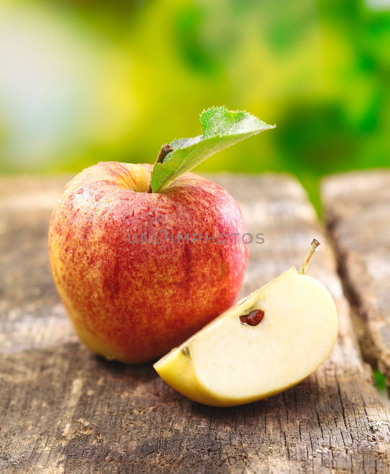 Quartered apple showing juicy the juicy flesh together with a whole fruit on an old textured wooden table outdoors