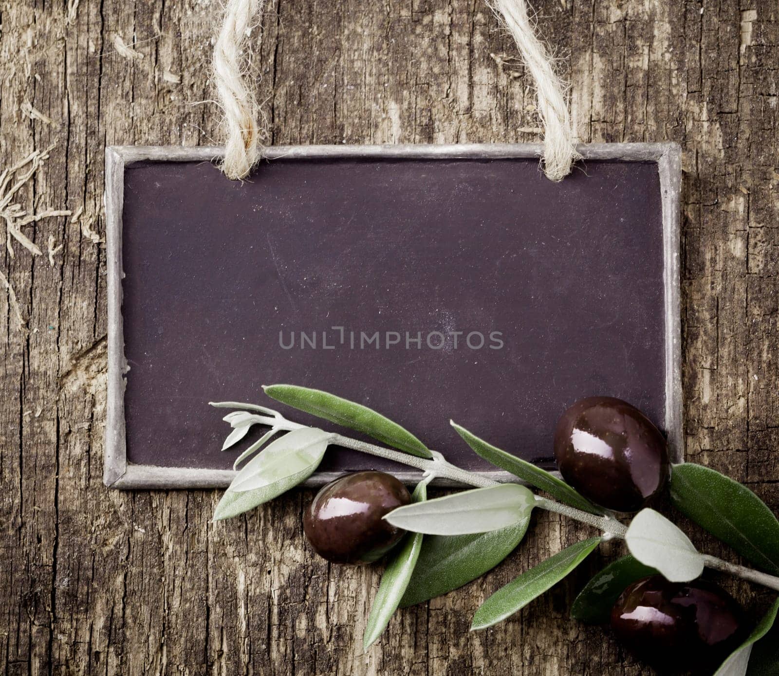 Fresh black olives on a leafy twig and a blank slate for your text lying on an old weathered wooden table