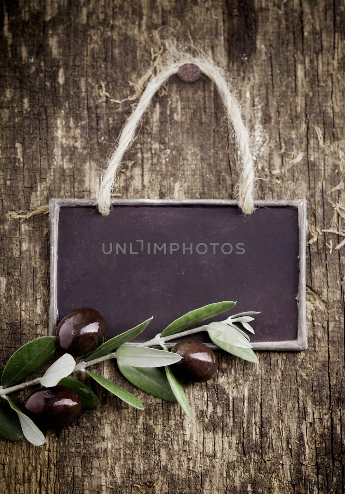 Fresh black olives lying with a slate blackboard on an old grungy weathered and textured wooden table