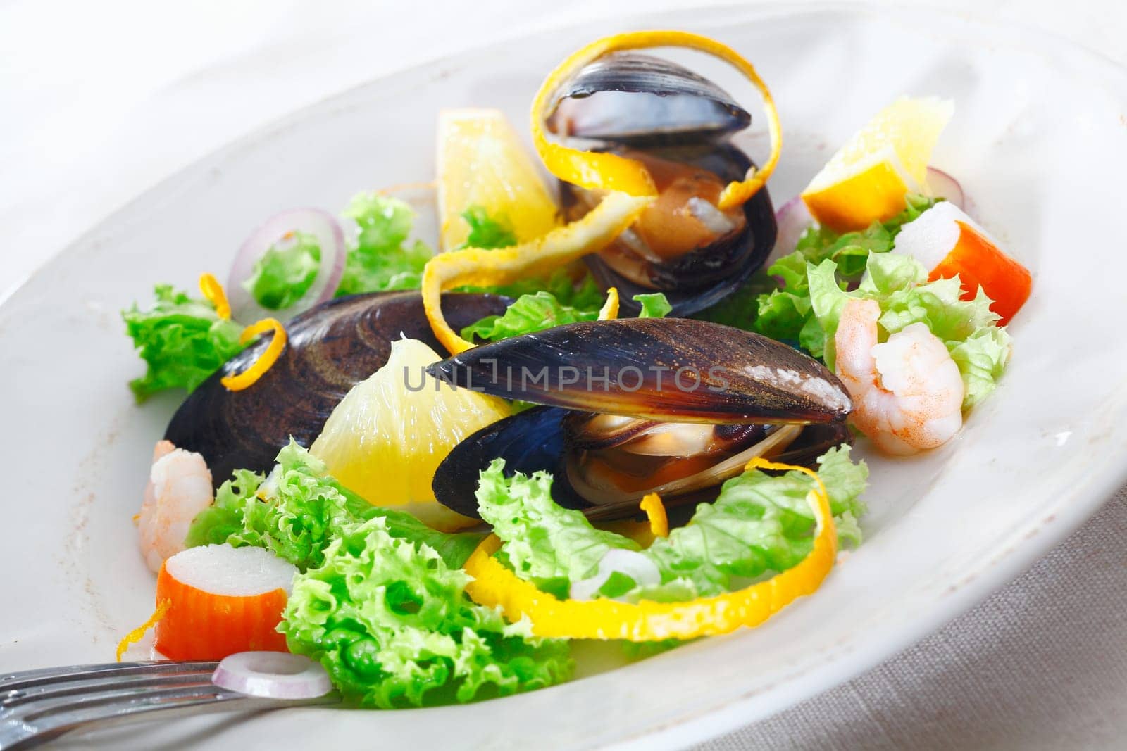 Serving of delicious seafood salad with mussels, crab and shrimp on a bed of crisp green lettuce garnished with orange peel