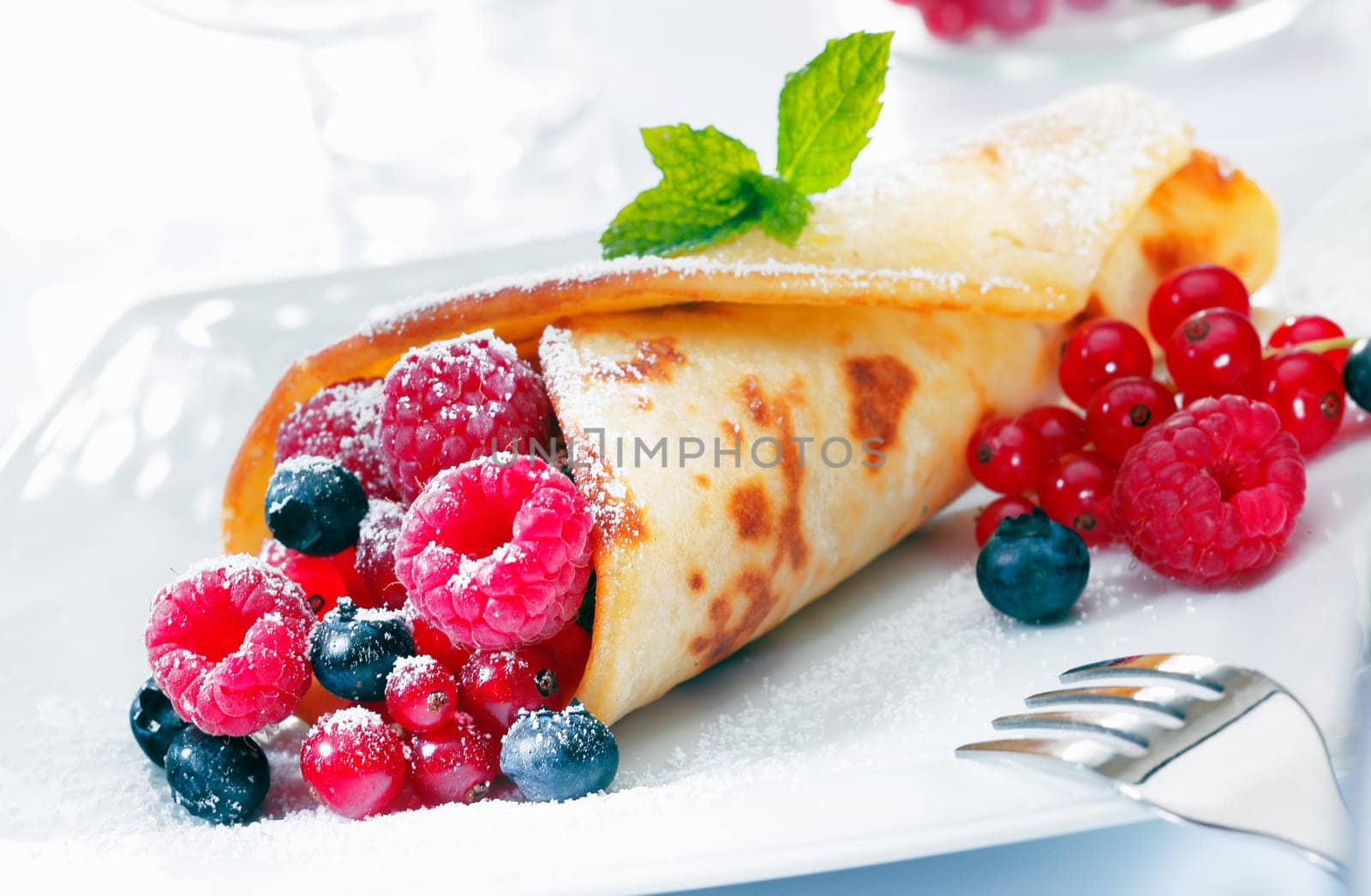 Scrumptious golden berry pancake filled to overflowing with raspberries, blueberries and redcurrant sprinkled with sugar
