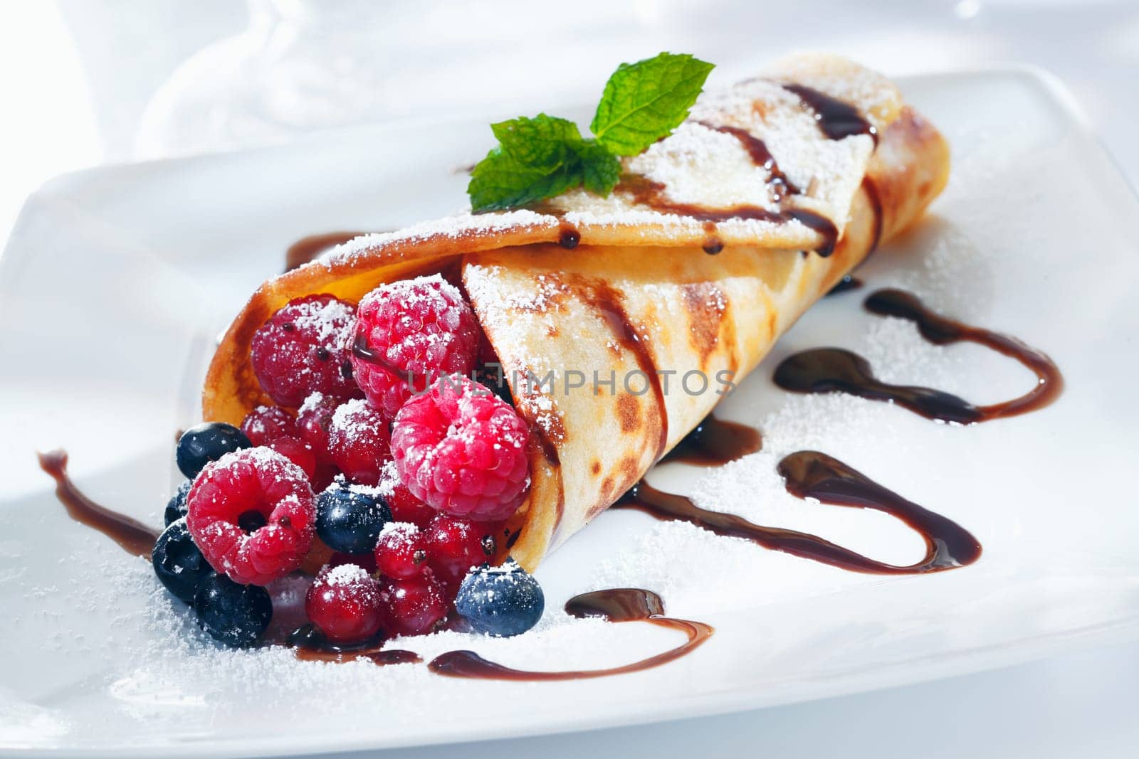 Fresh fried golden pancake filled with an assortment of berries drizzled with chocolate and garnished with mint