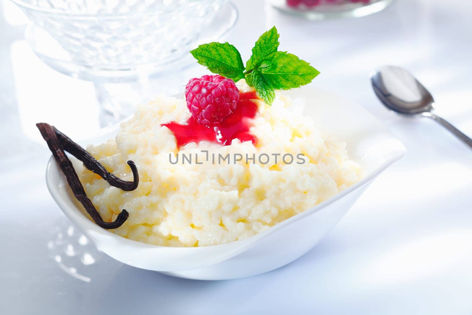 Fruity rice pudding dessert with raspberry topping and vanilla pods on white background.