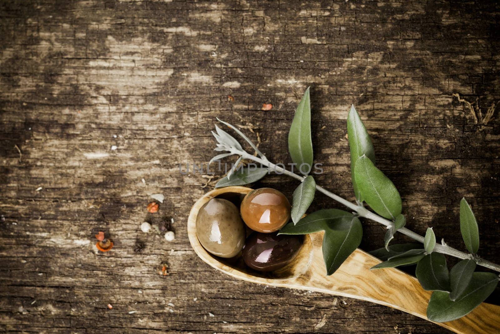 Fresh olives in a wooden spoon on a grungy textured rustic wood table with copyspace