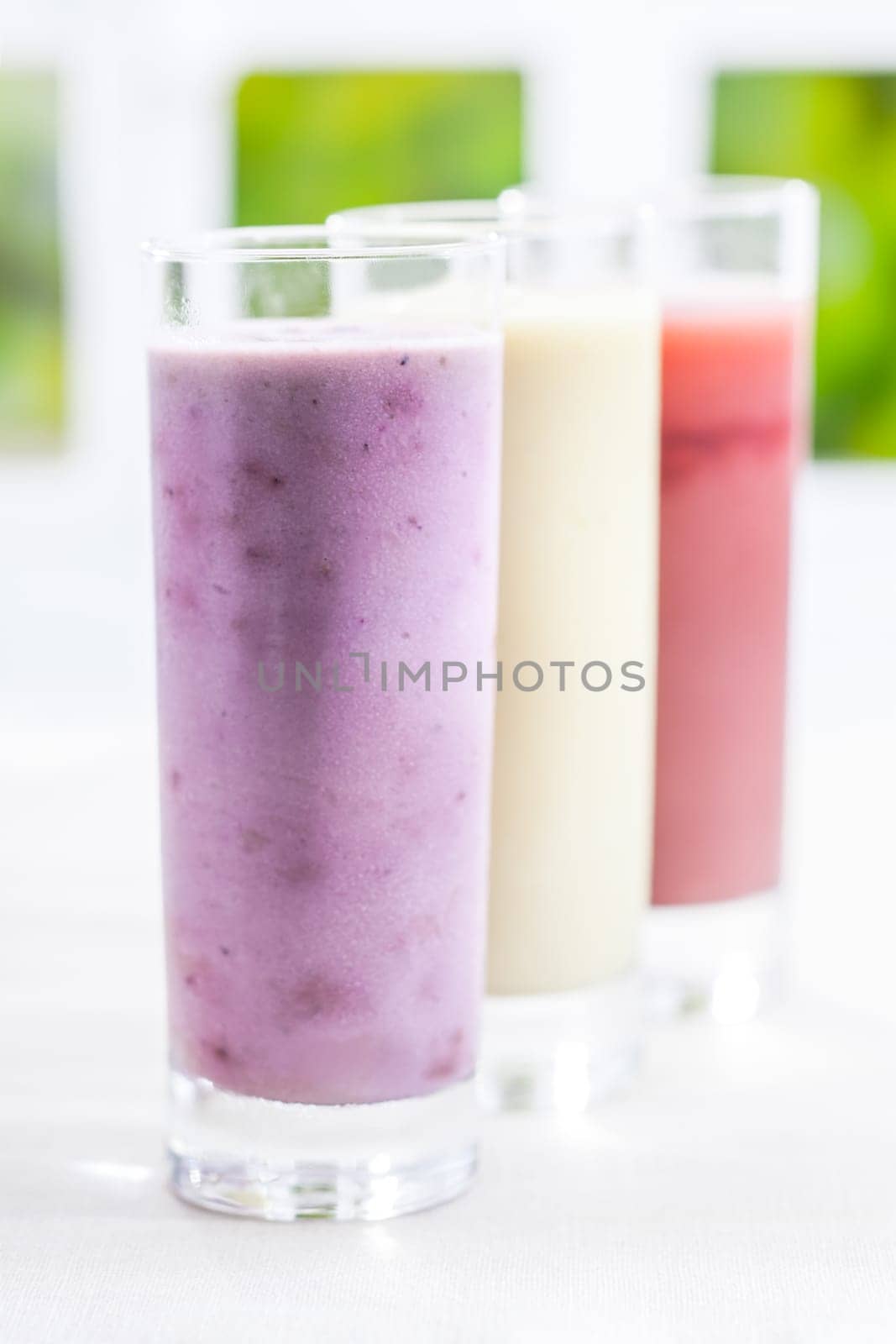 A tall glass of creamy blended yoghurt berry smoothie with a variety of other flavours in a receding row with shallow dof