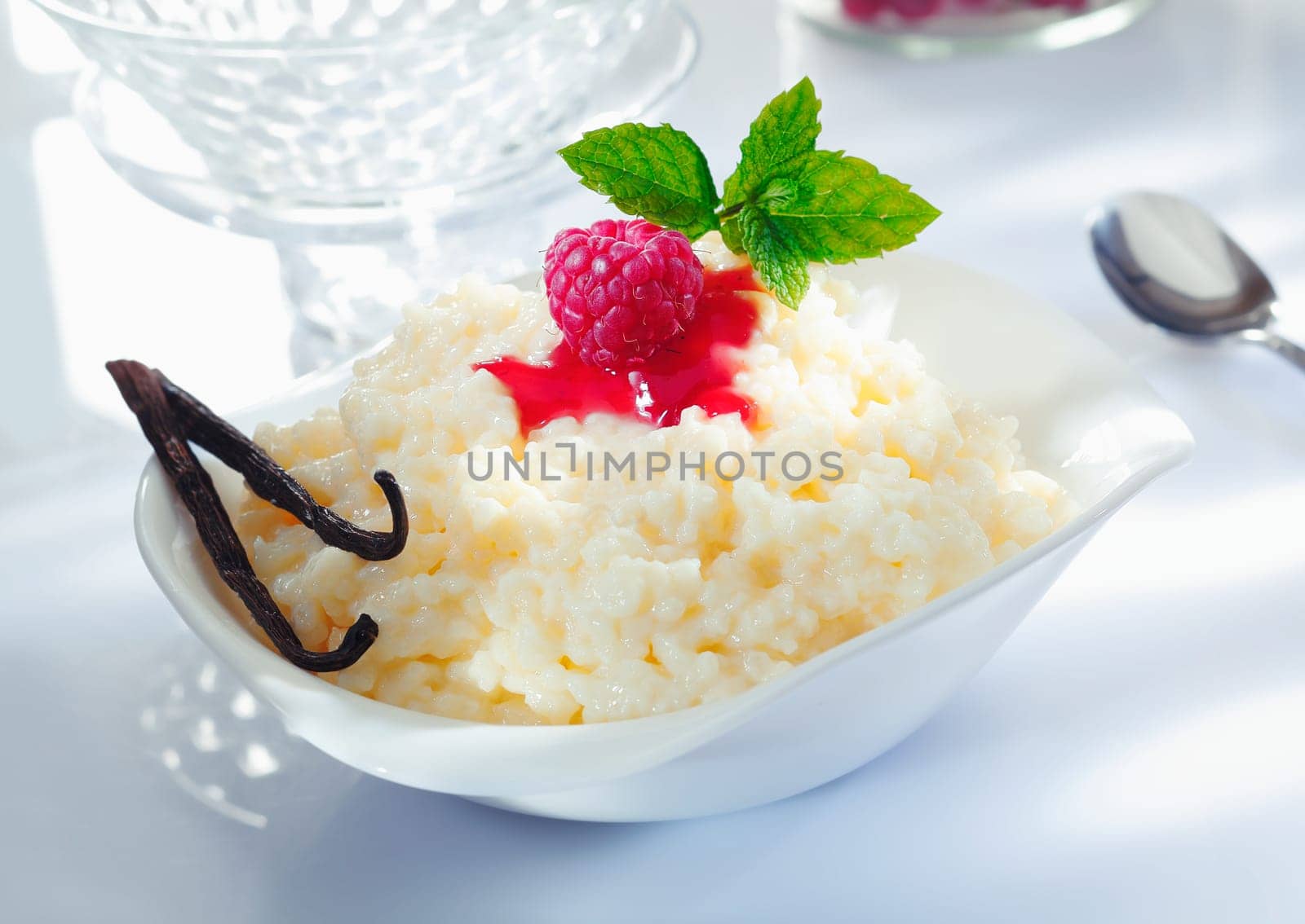 Scrumptious creamy rice dessert topped with raspberry and garnished with vanilla pods served on a luxury dinner table