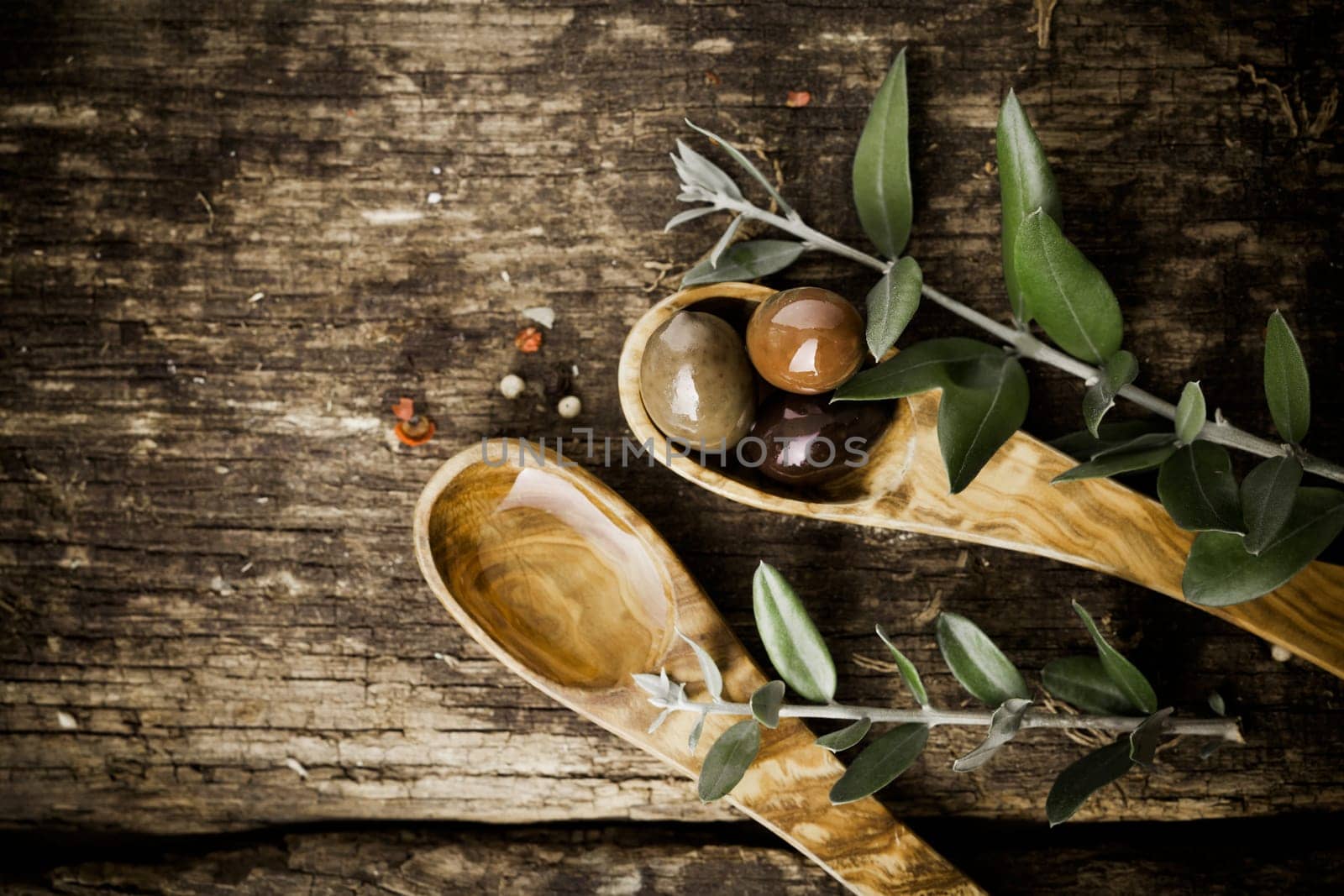 Olive wood spoons with fresh olives and leaves on an old grungy textured wooden tabletop with copyspace