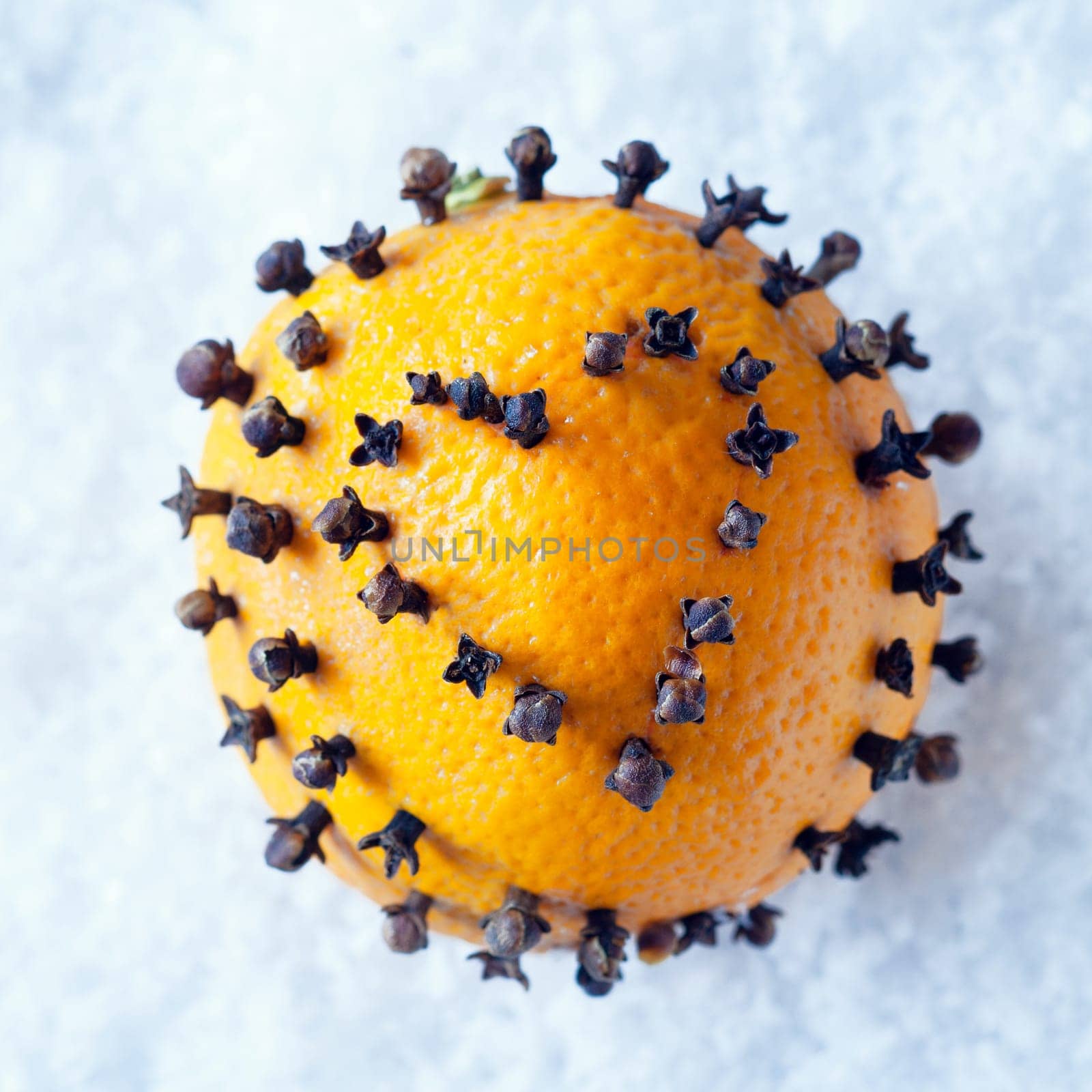 Christmas decoration of a fresh whole orange with a spicy clove heart decoration piercing the skin lying on a bed of snow