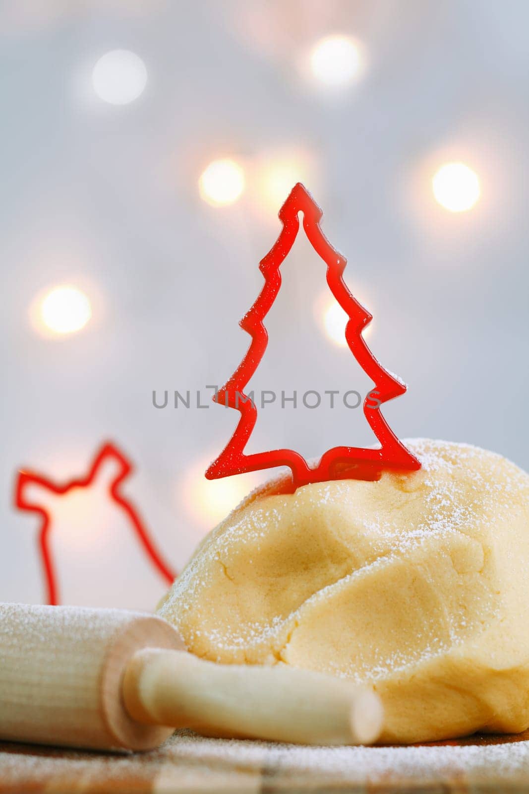 A red cookie cutter in the shape of a Christmas tree tops a freshly made mound of pastry dough while preparing Christmas cookies