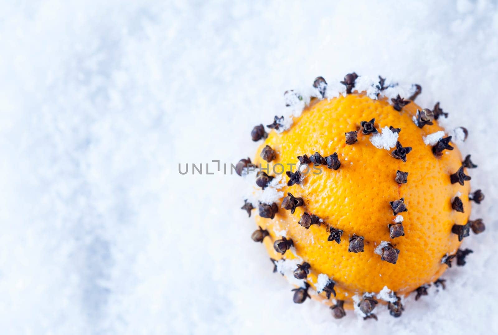 A fresh ripe orange decorated with cloves piercing the skin in the symbolic shape of a heart to celebrate Christmas nestling on snow with copyspace