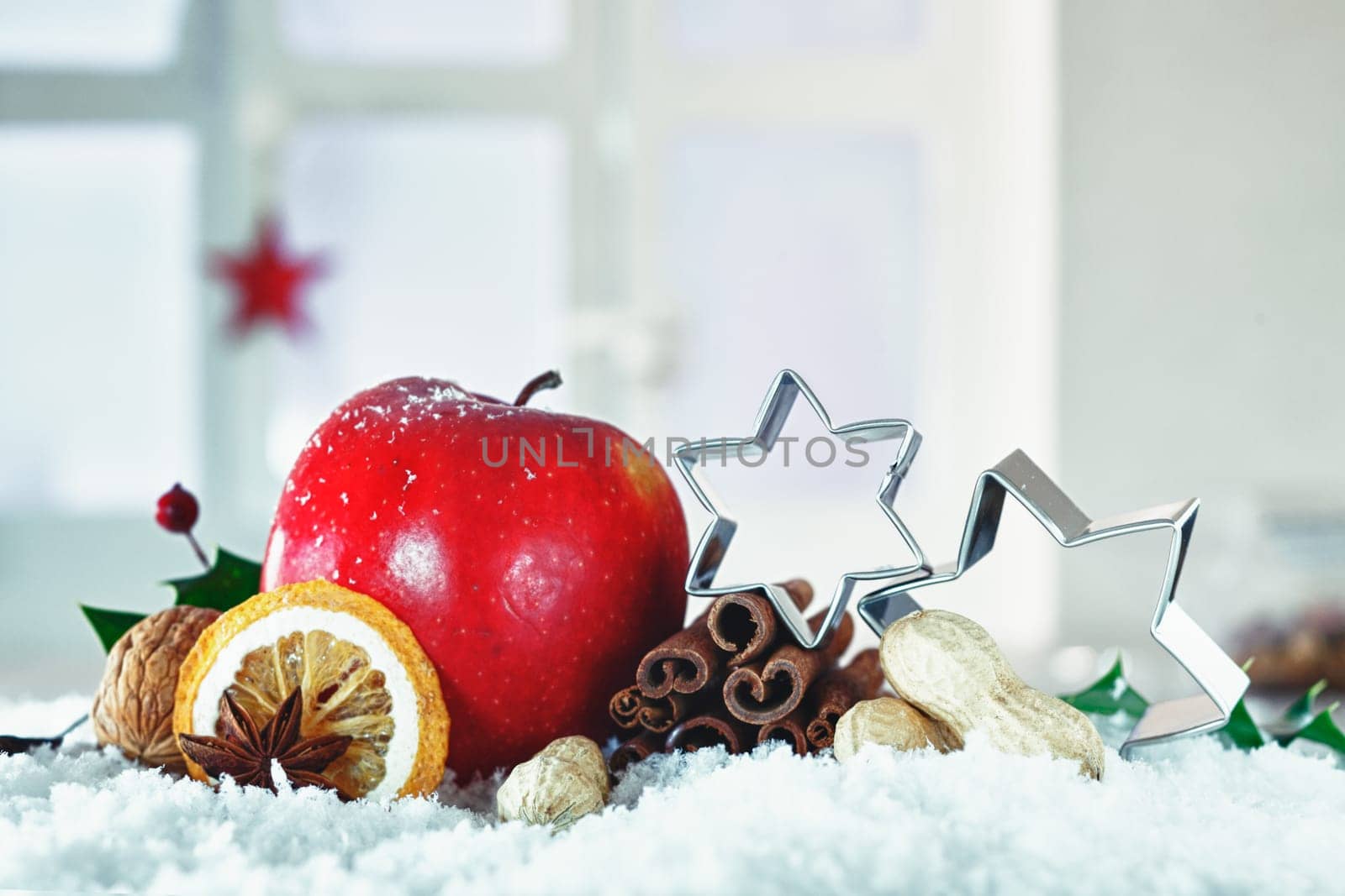 Beautiful Christmas still life with stars balanced on dried fruit, nuts and spices and a festive red apple nestling in snow with copyspace