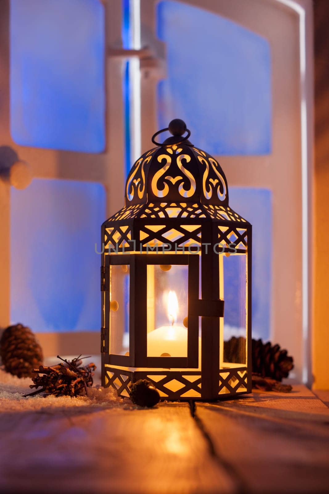 Ornamental Christmas lantern with a glowing candle illuminating a window in the evening light