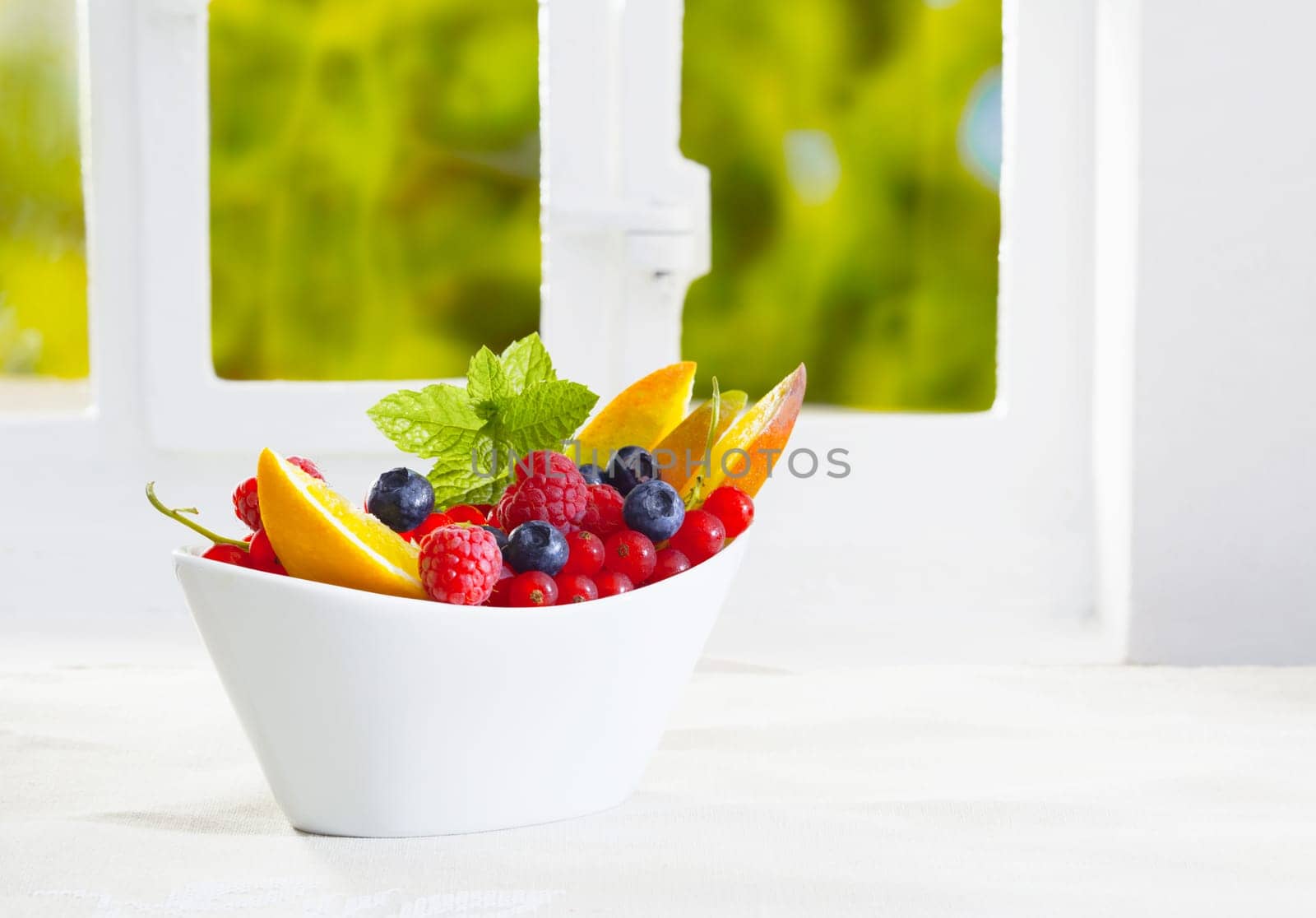 Colourful bowl of tropical fruit with an assortment of raspberries, blueberries, redcurrant and sliced oranges garnished with fresh green mint with copyspace
