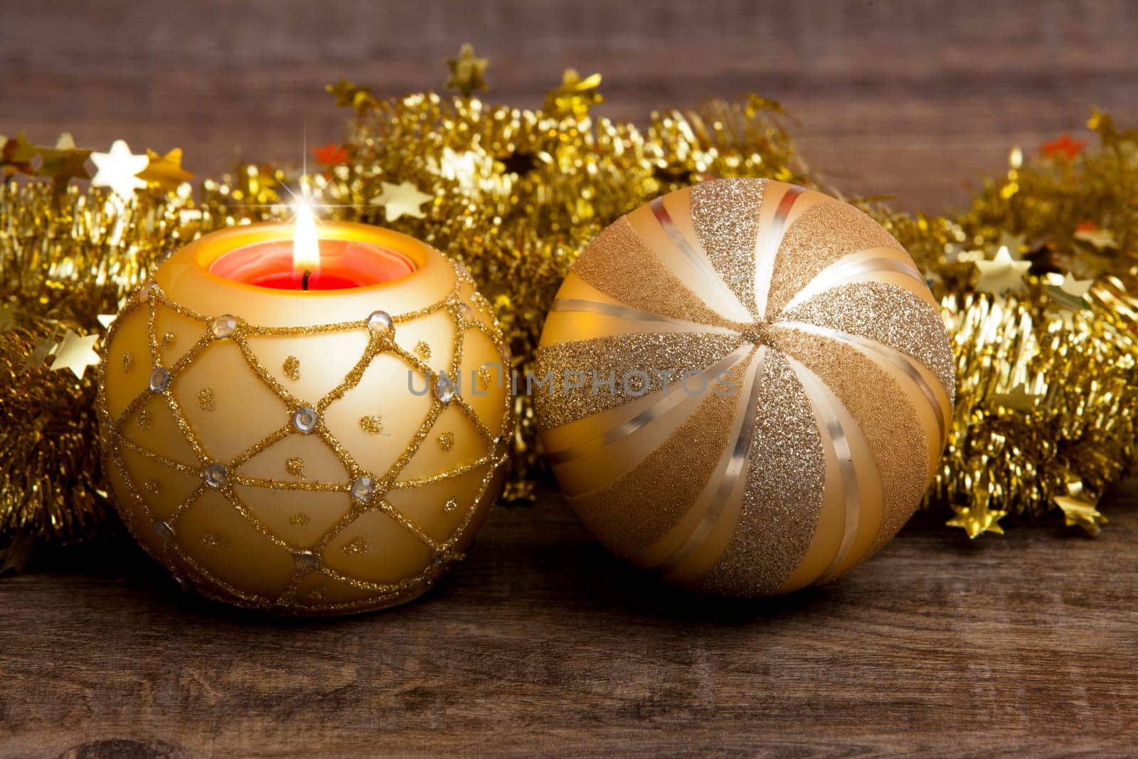Candle in golden candle holder and golden Christmas tree ball with gold garland on wooden background