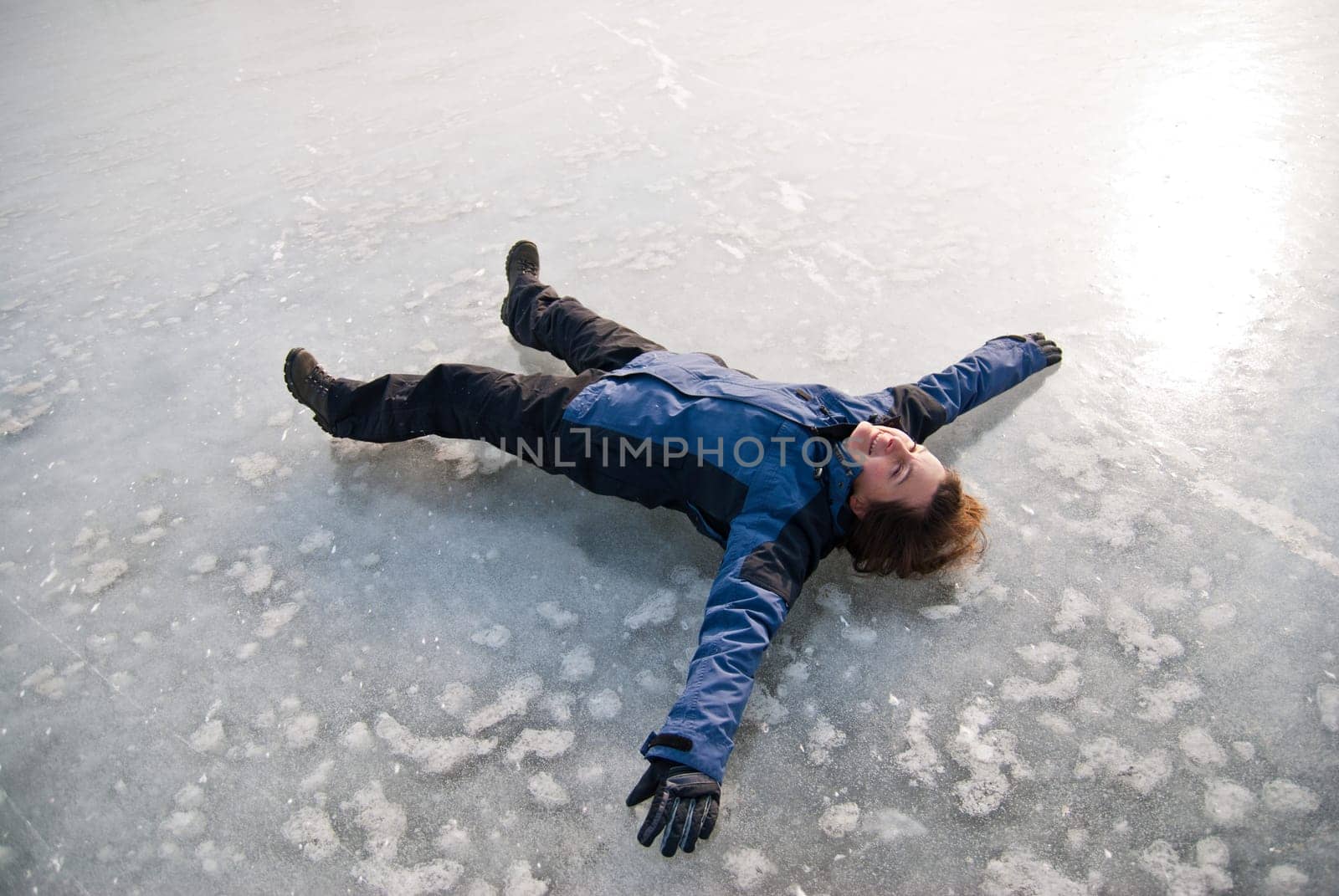 Young smiling woman is lying on ice (frozen lake) - winter outdoor scene