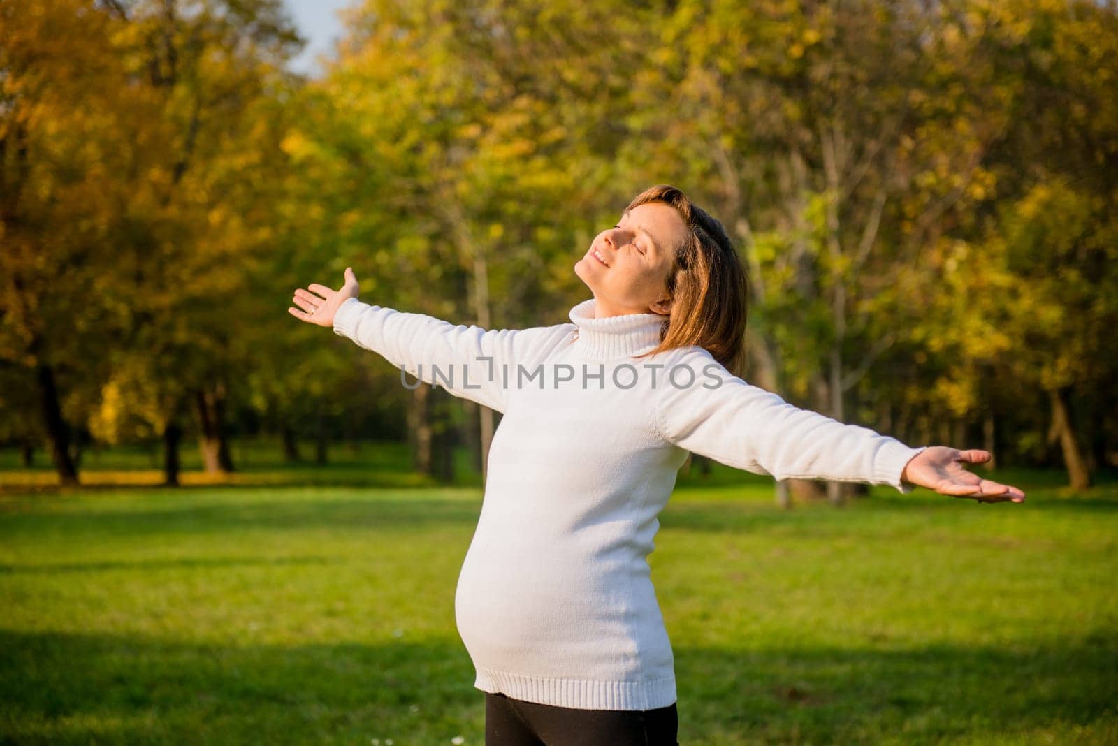Happy pregnant woman enjoying life outdoors in autumn colorful nature