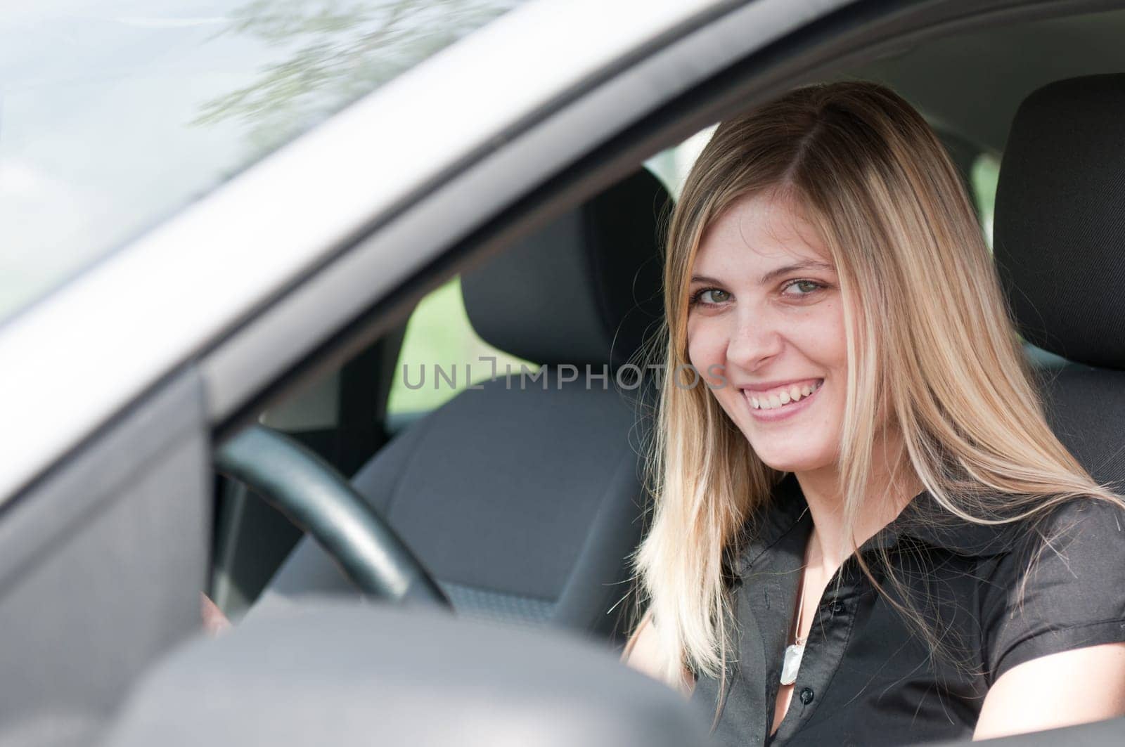 Young beautiful smiling woman driving car - portrait through side window