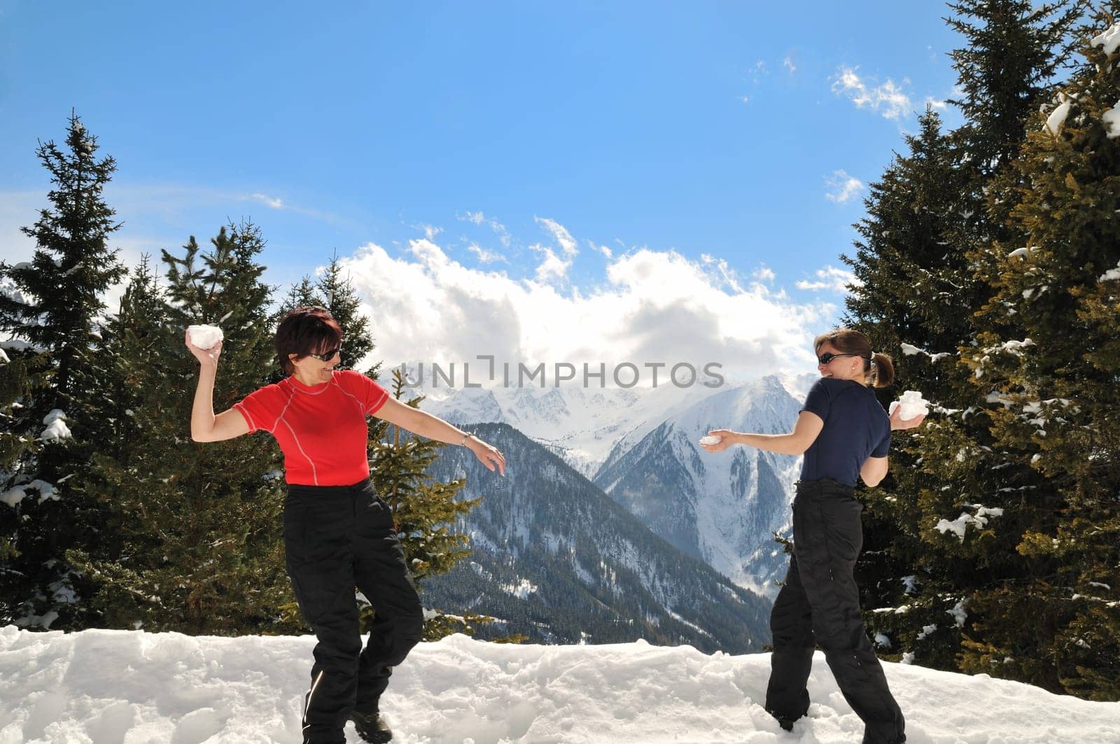 Senior woman throws snowball on her daughter - winter mature people series