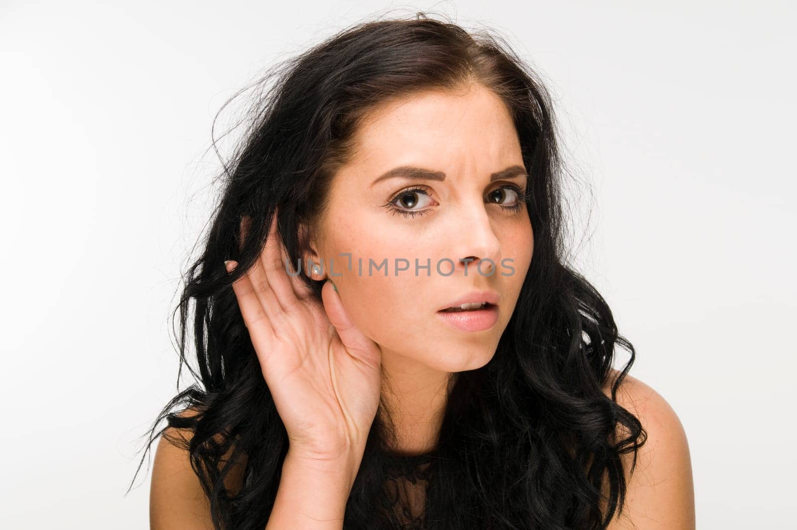 Frontal head and shoulders shot of young black-haired woman against white background and hands on ears symbolizing hearing loss
