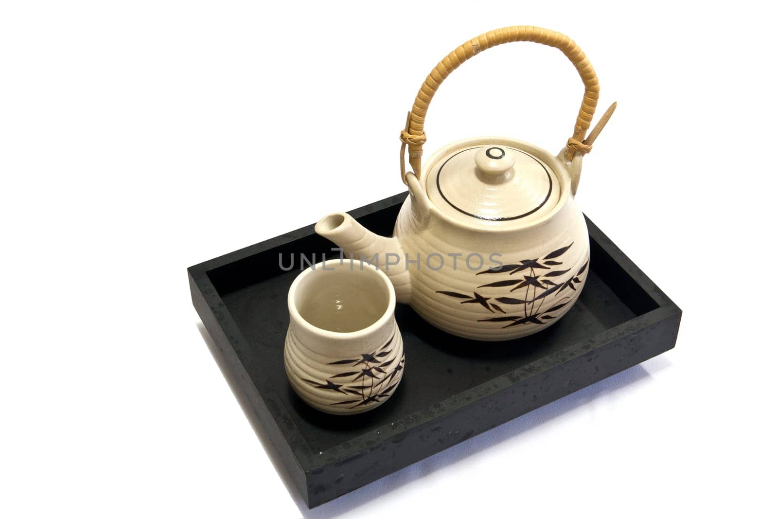 Teapot and teacup painting bamboo leaves on a black tray.