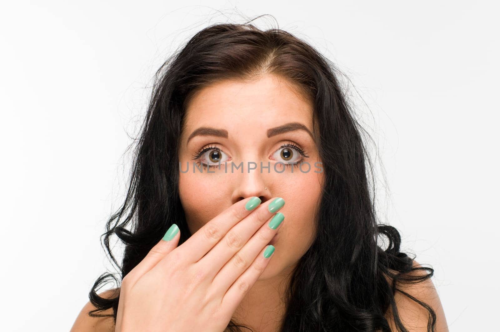 Head and shoulders shot of a young black-haired woman against a white background covering her mouth with one hand