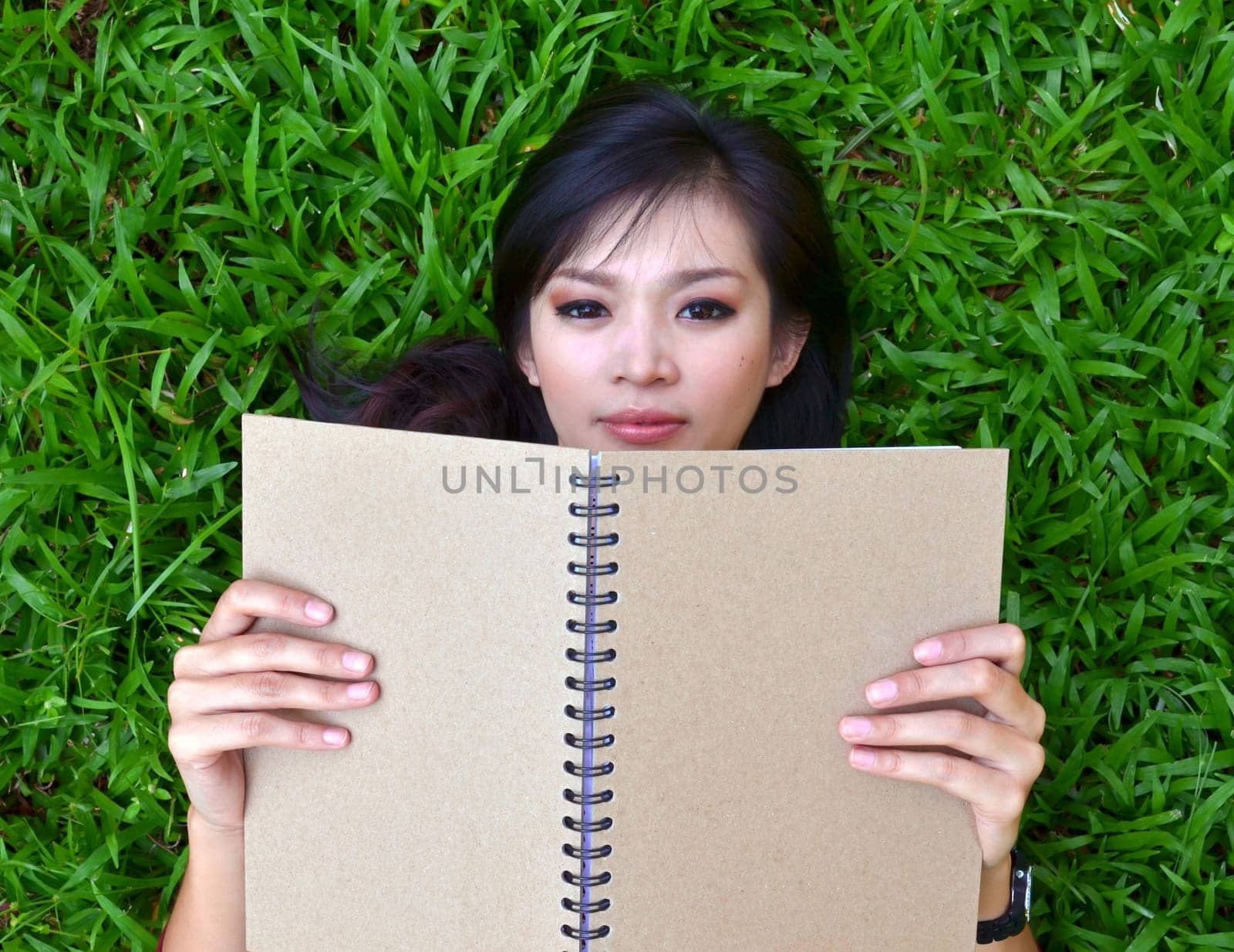 Woman lying on green grass with a book
