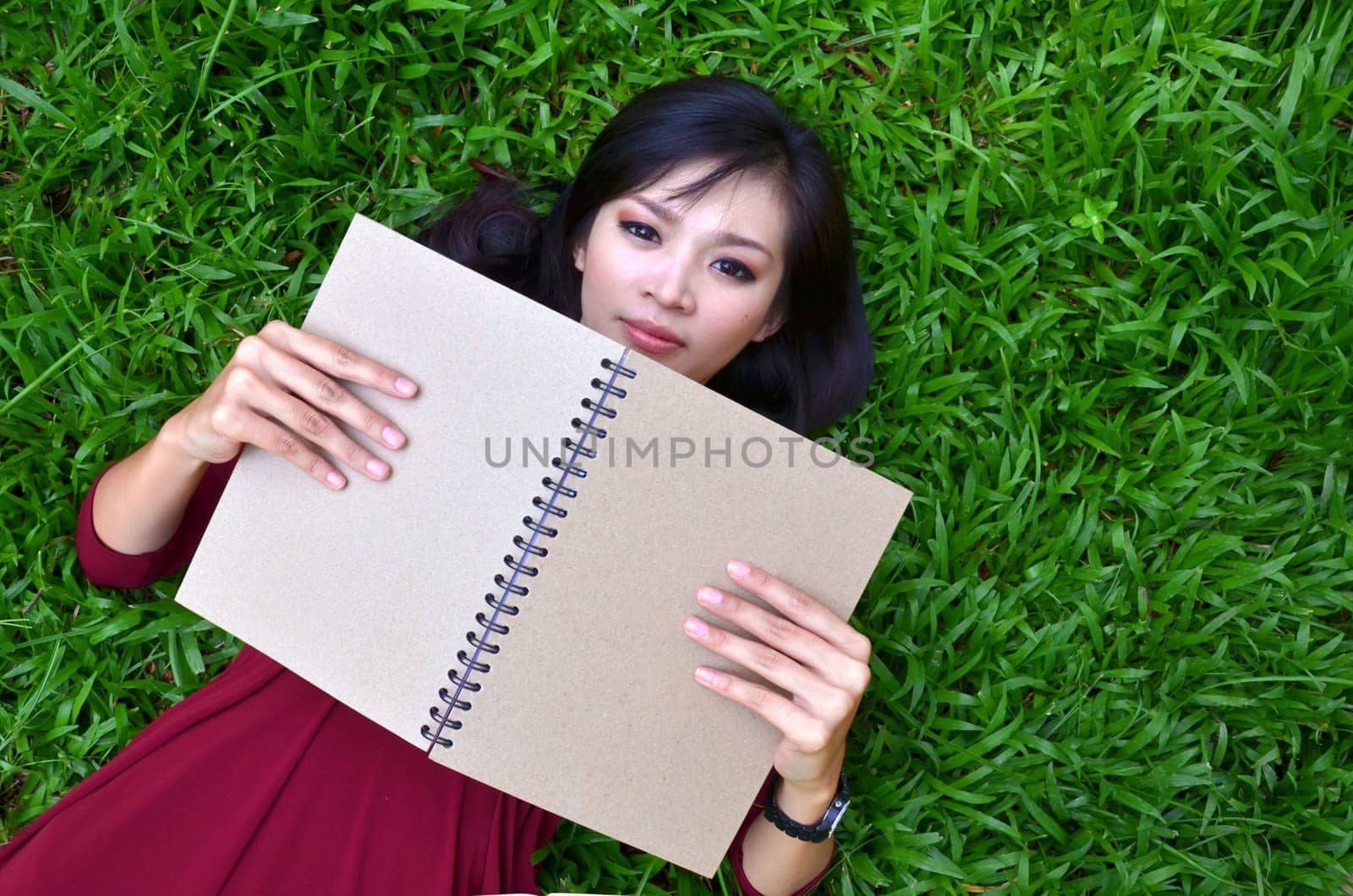 Woman lying on green grass with a book