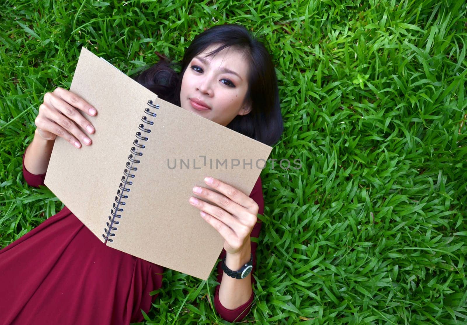 Woman lying on green grass with a book