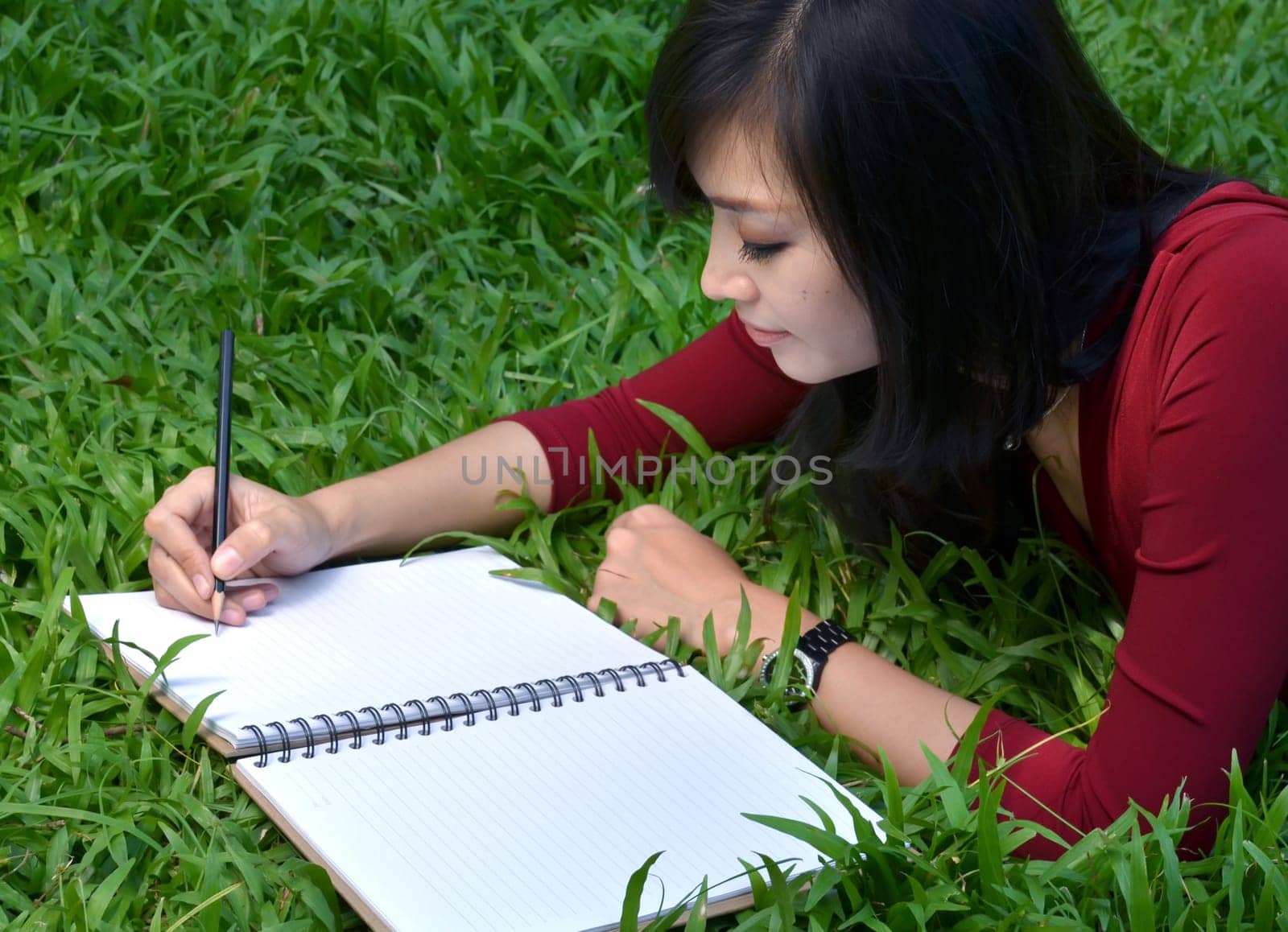 pretty women lying on green grass and writing book