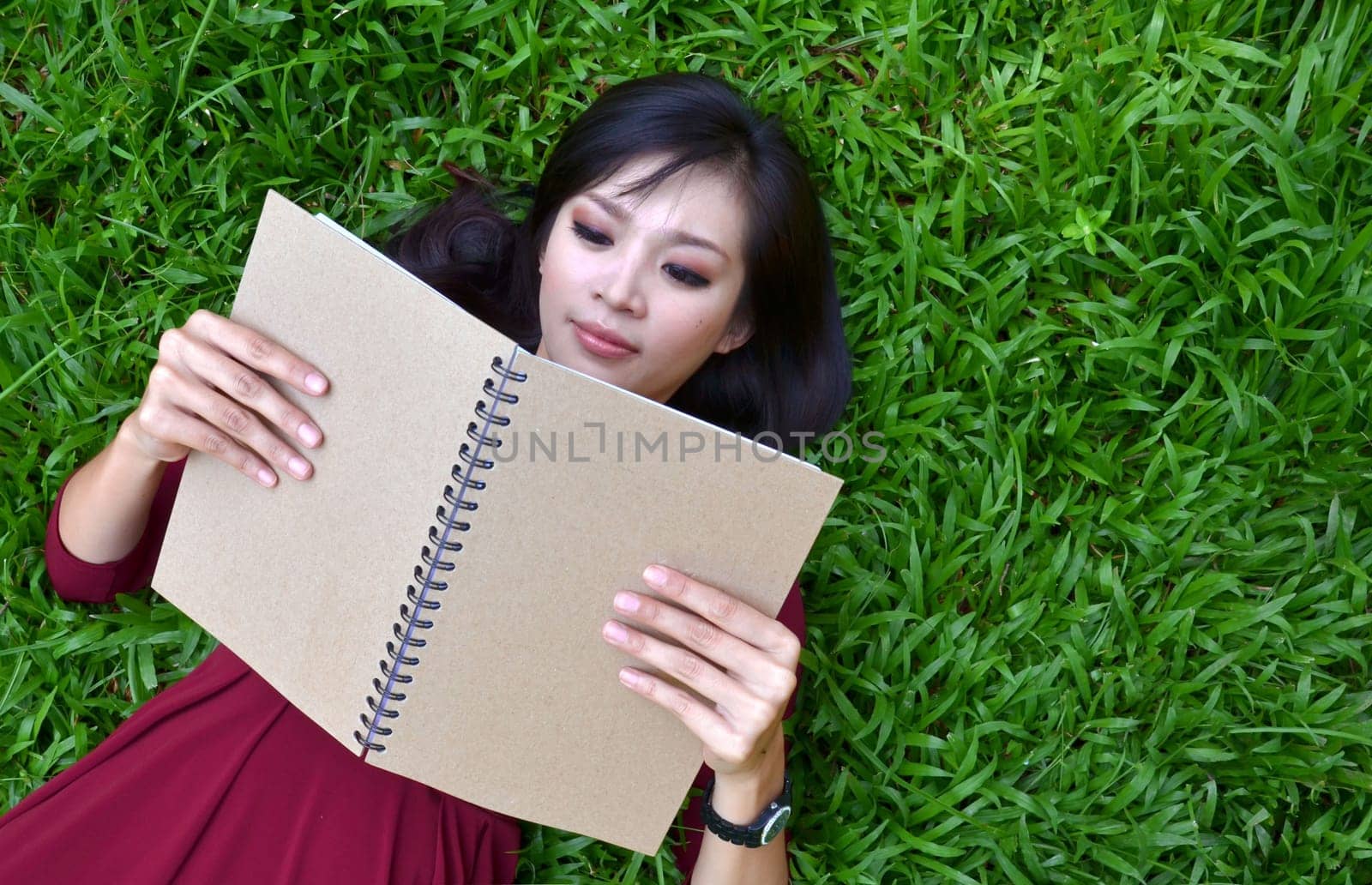 Woman lying on green grass with a book