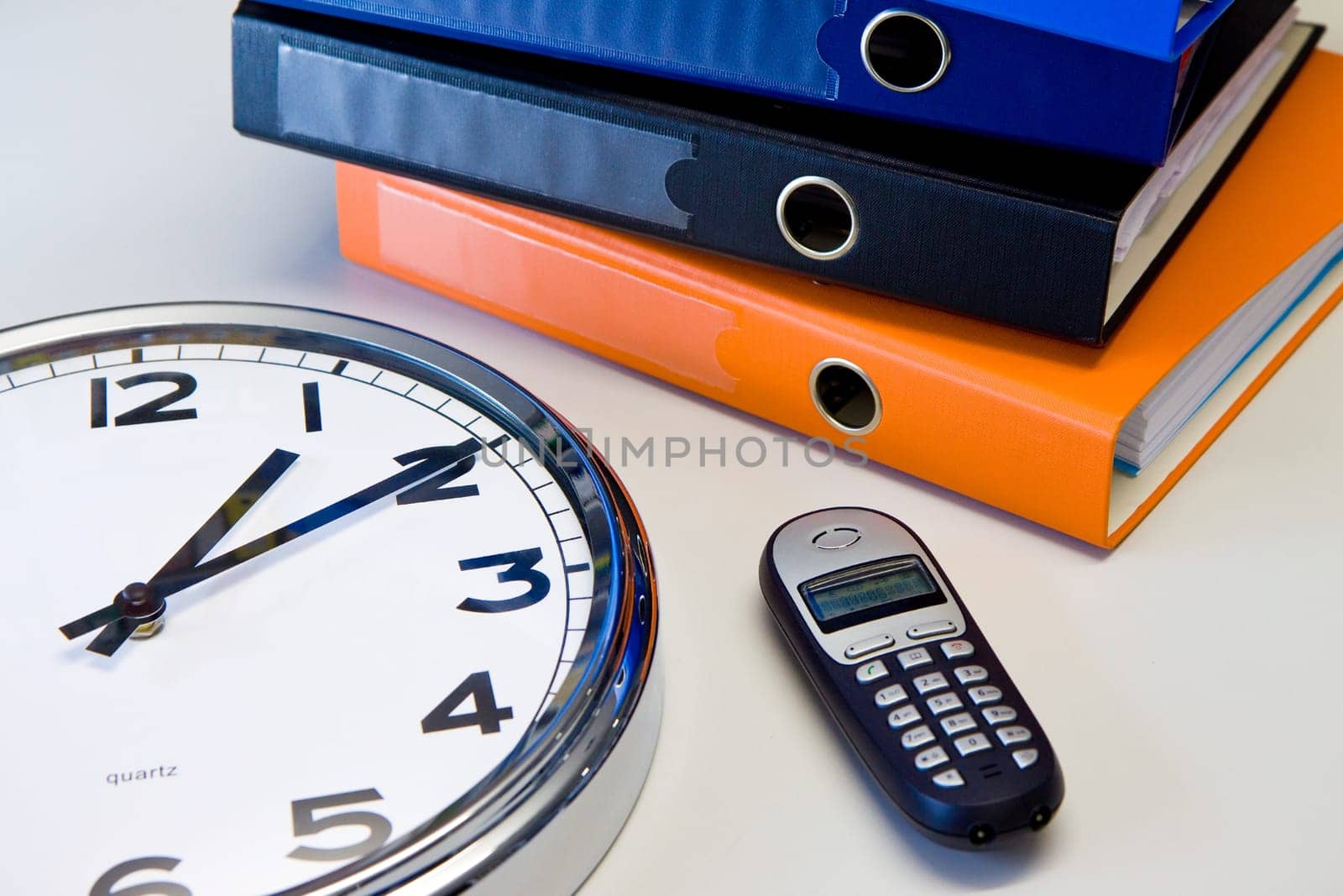 Clock, phone and color binders on the office desk,
