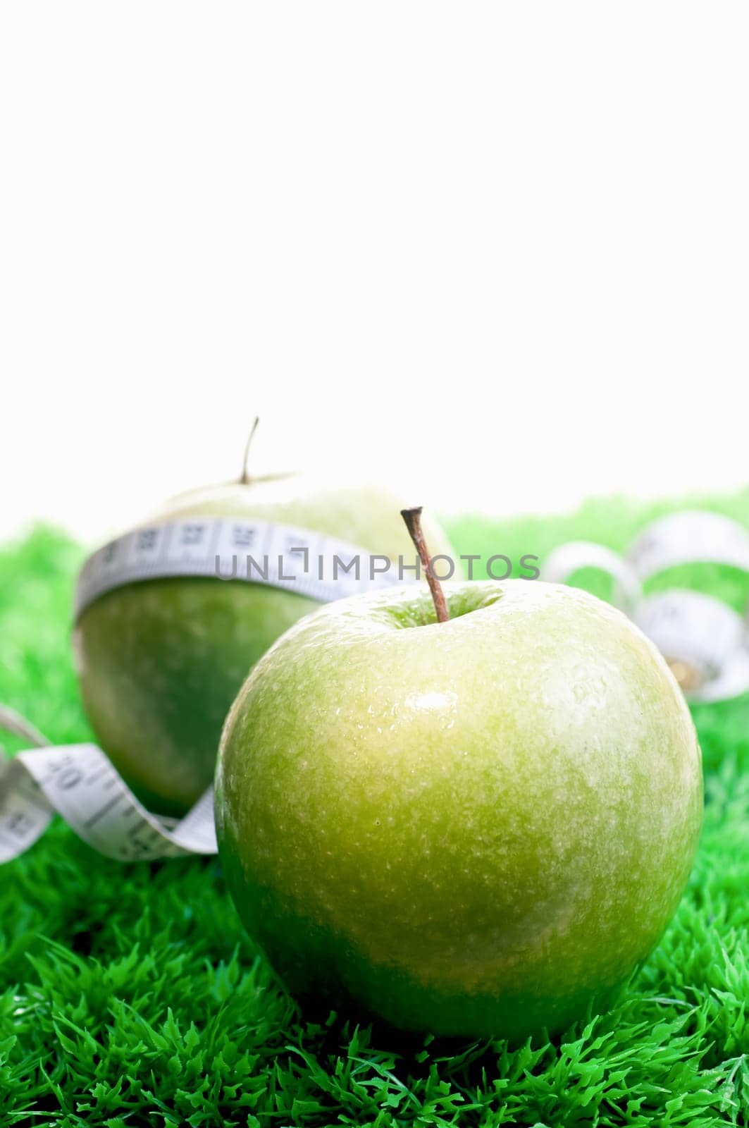 Two apples close up on the grass and one with a tape measure