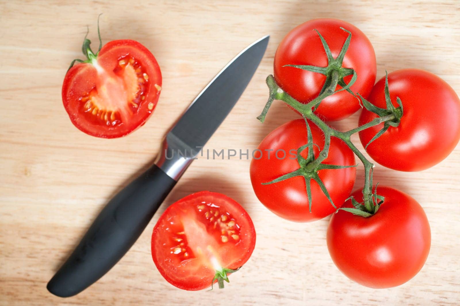 Fresh tomatoes being sliced on a wooden chopping board with knife
