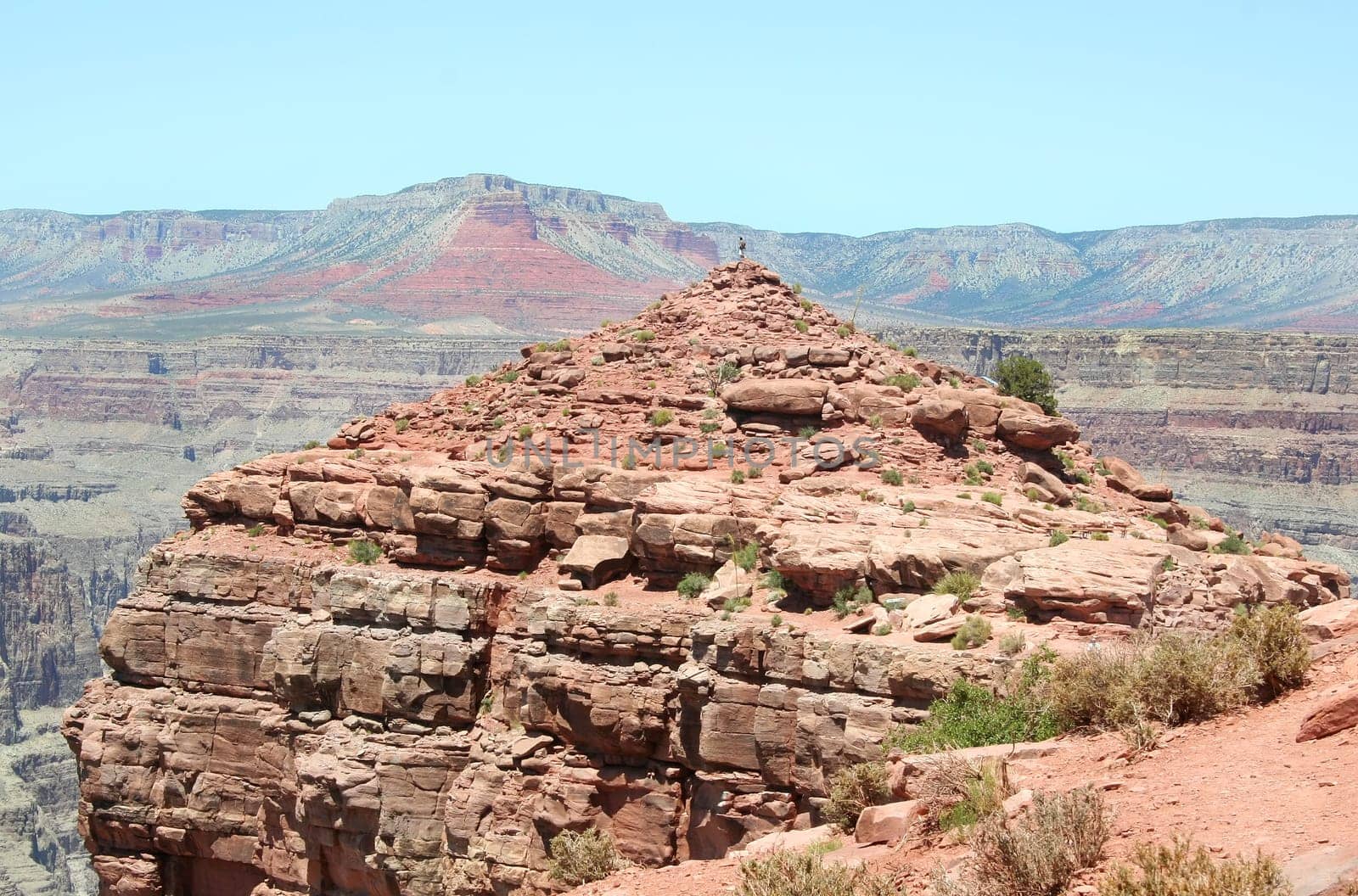 Person standing on top of the rocky knoll at Guano Point on the West Rim of the Grand Canyon.
