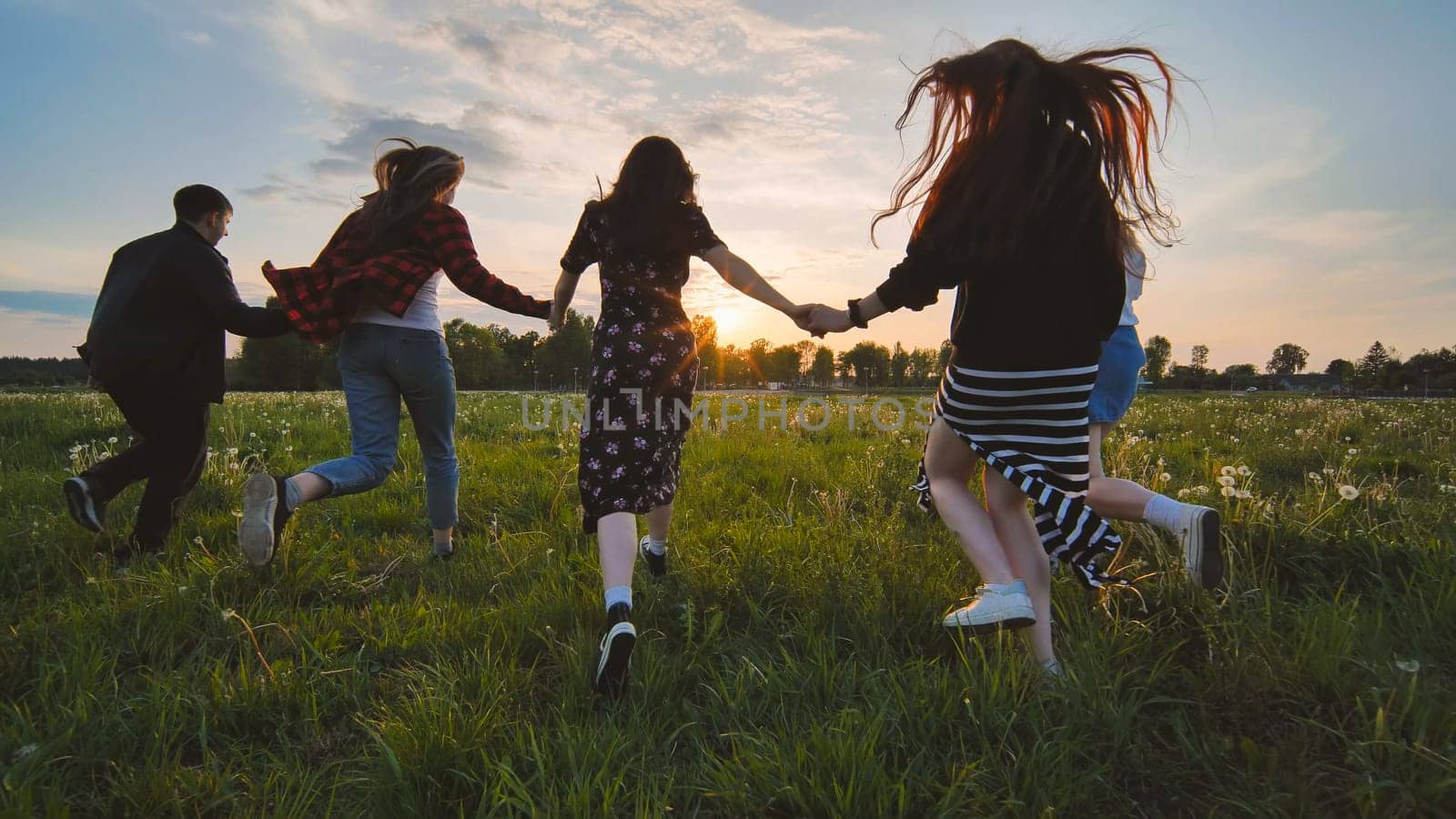 Cheerful friends run to meet the sun holding hands